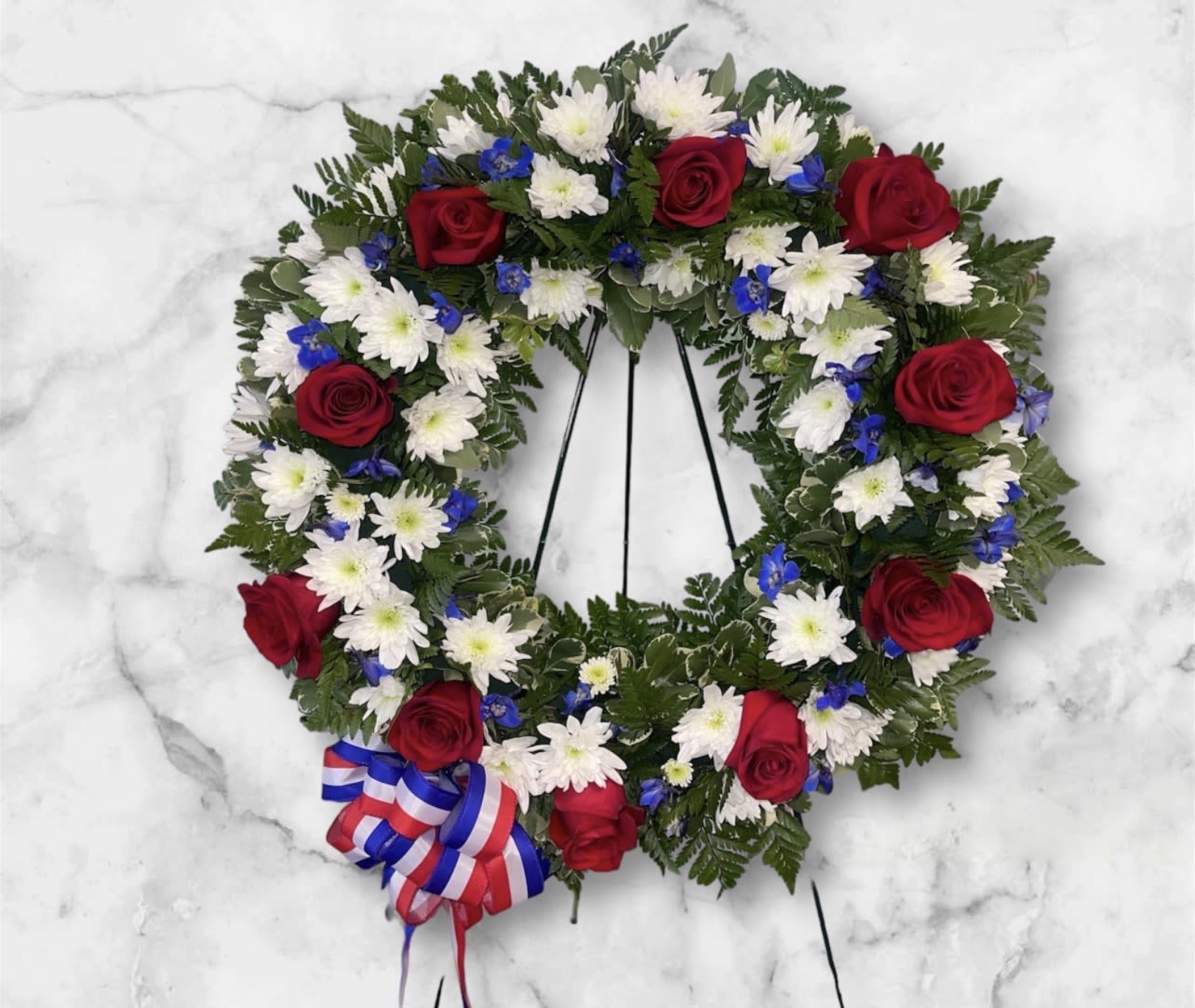 Heart-shaped floral wreath with red roses, white daisies, and blue accents