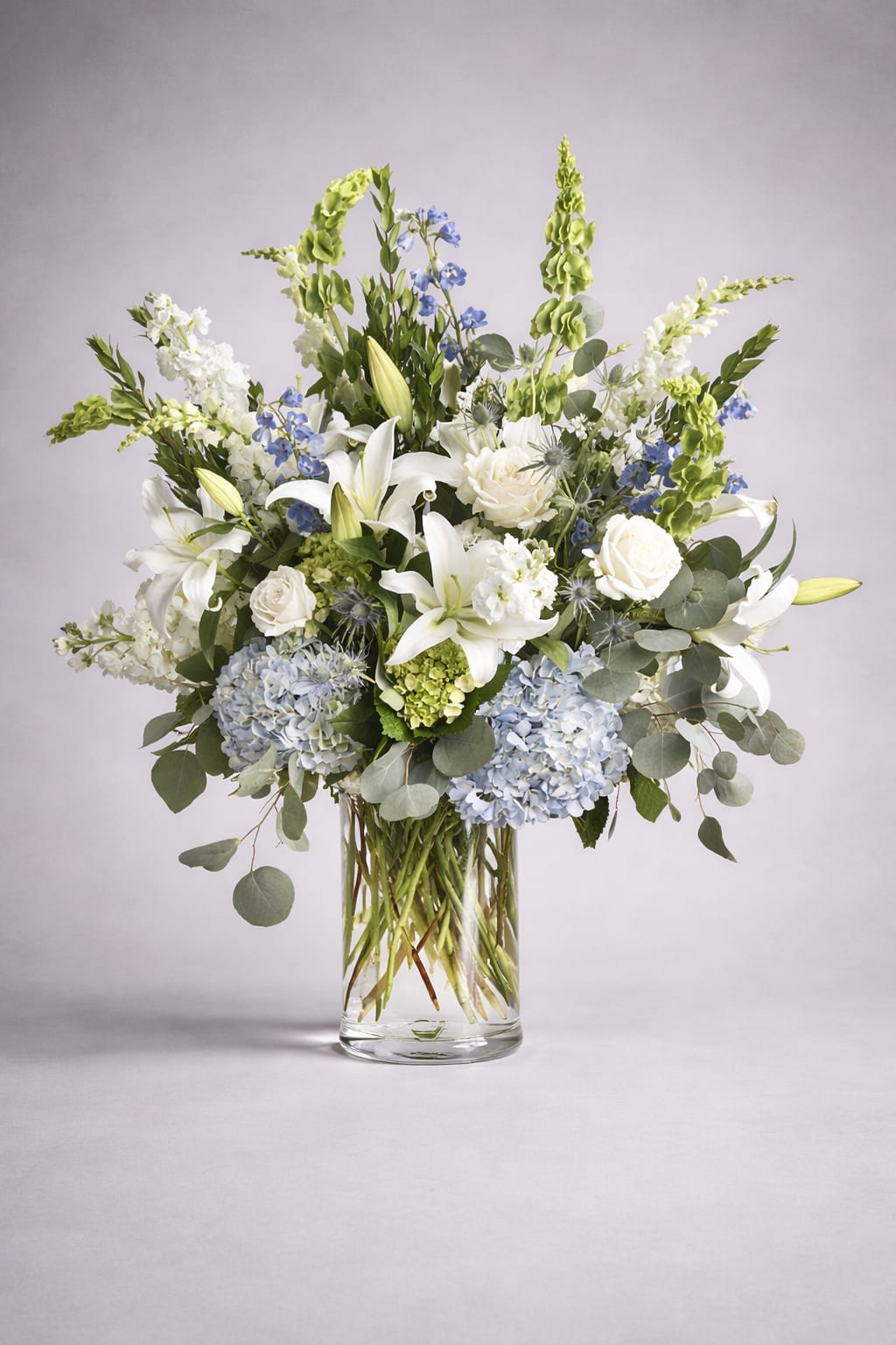 White lilies and blue flowers in a clear glass vase
