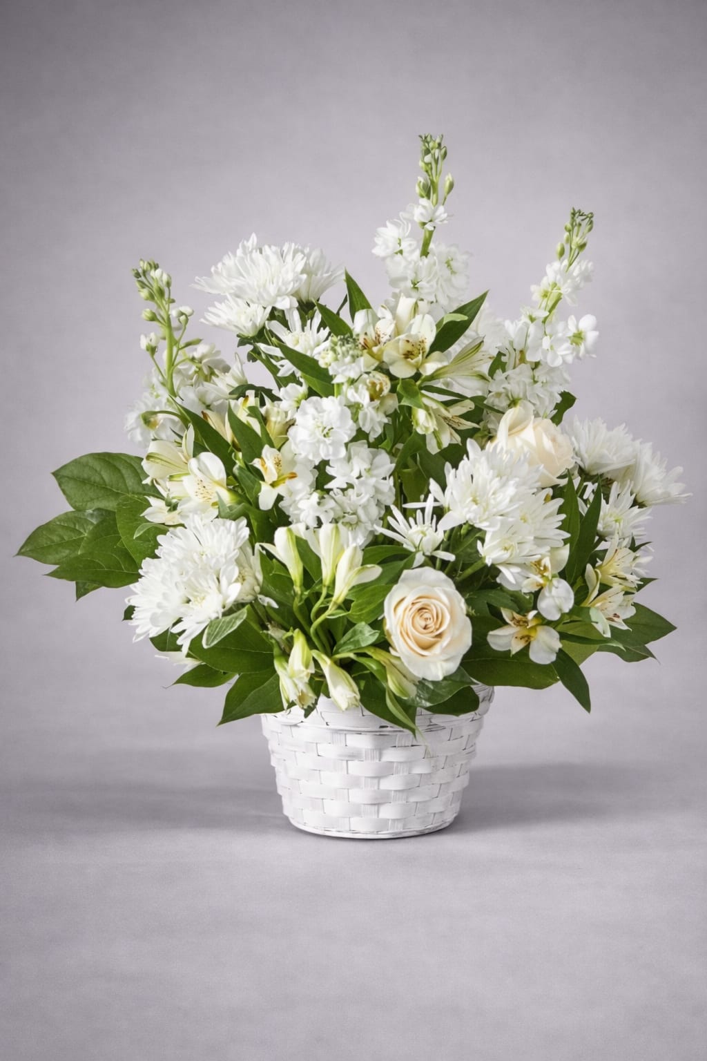 White floral arrangement in a white woven basket with green foliage