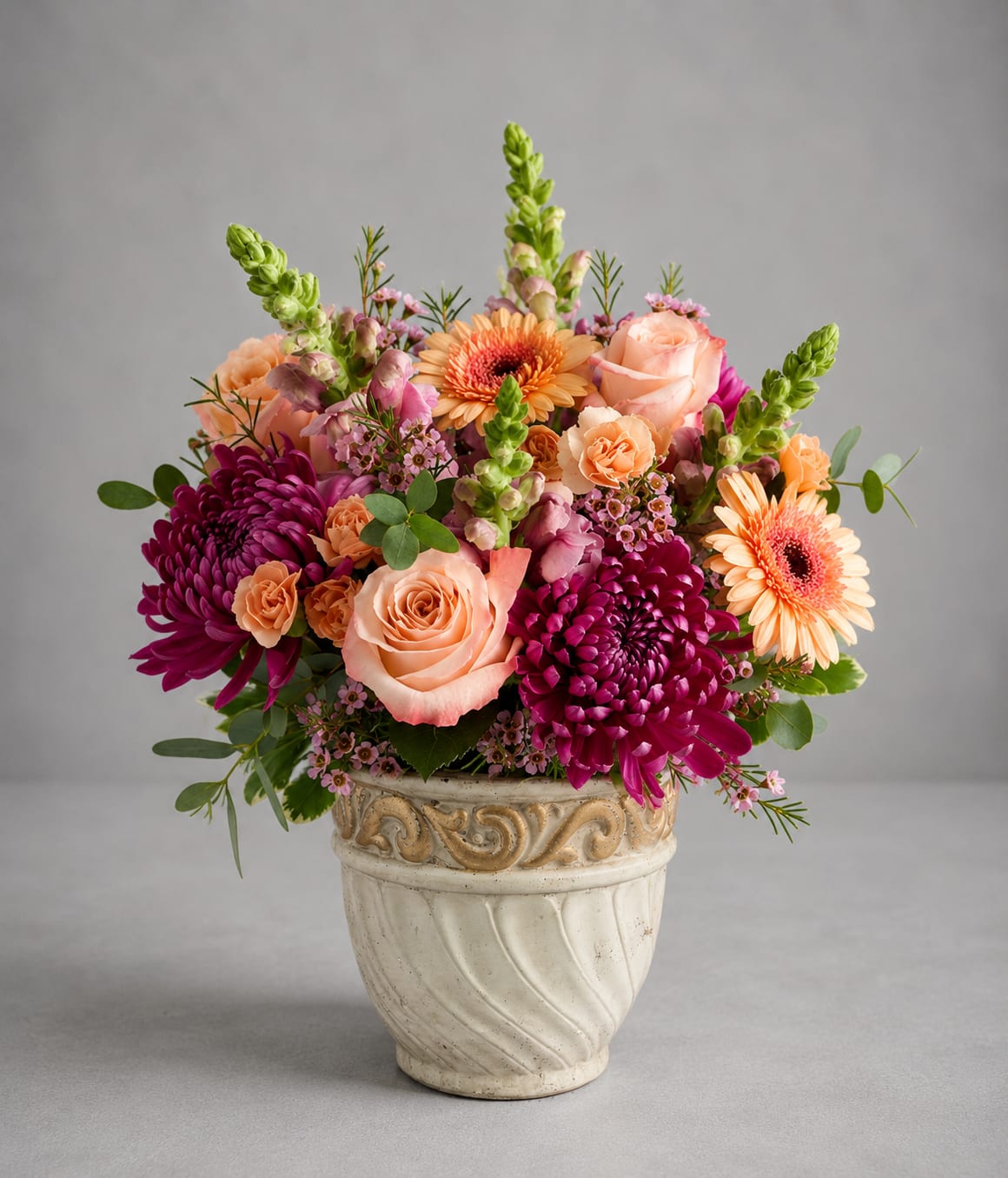 Mixed bouquet of peach, pink, and purple flowers in a decorative ceramic pot