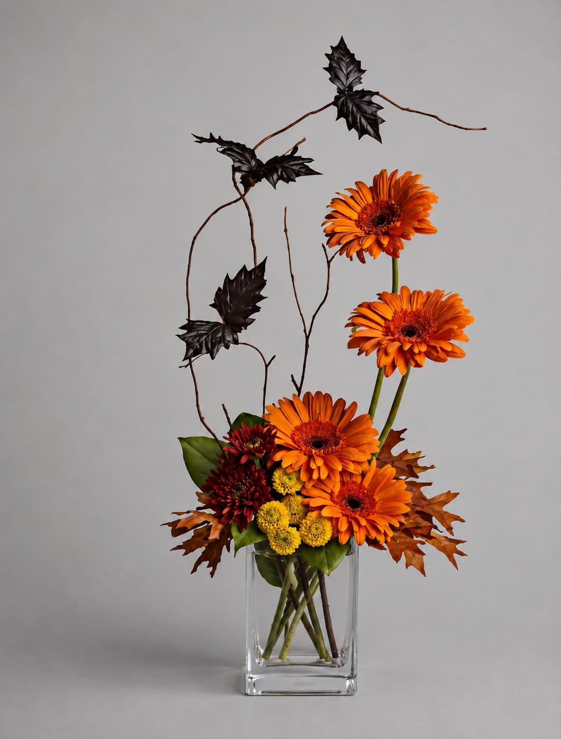 Orange gerbera daisies in a clear glass vase with autumn leaves