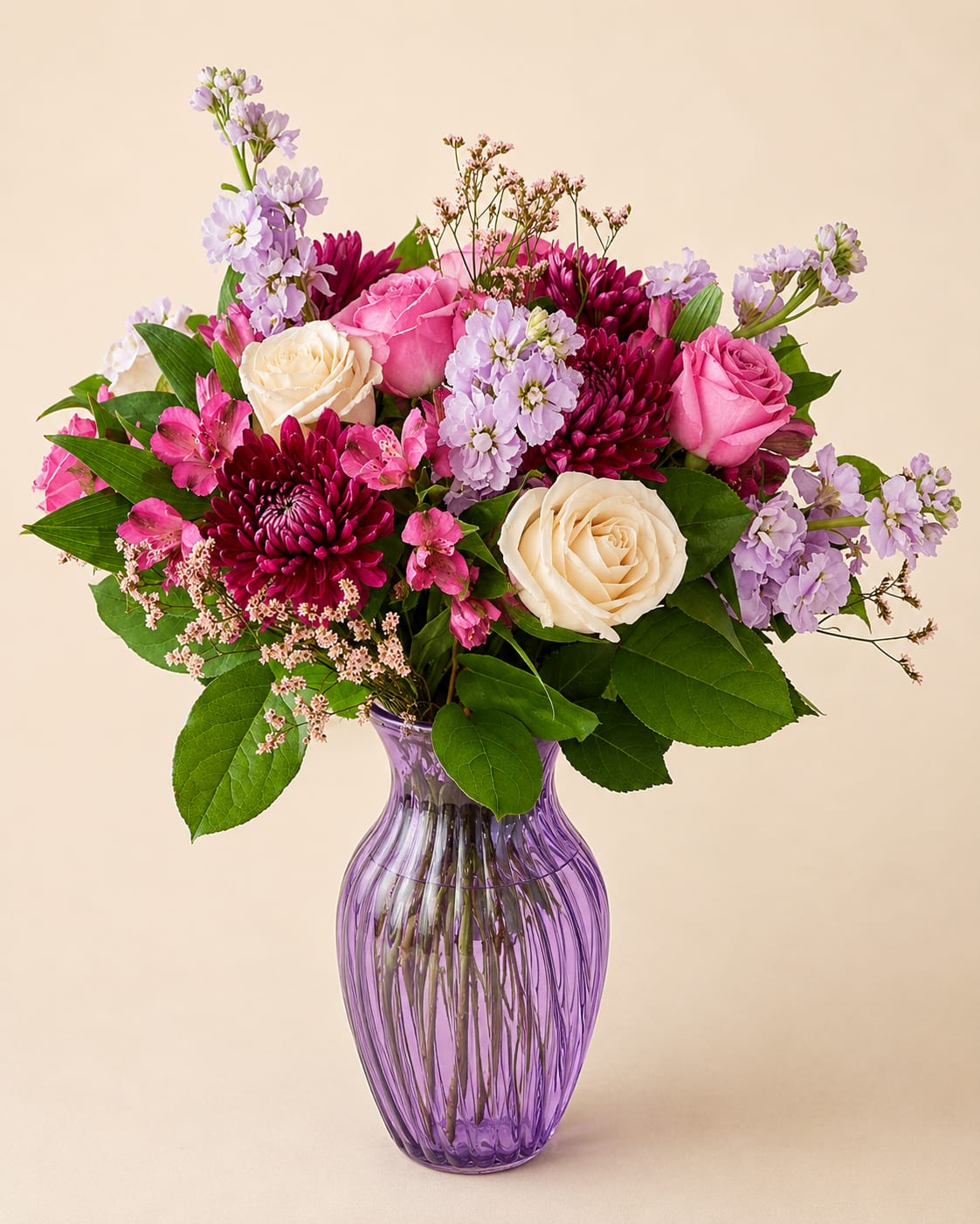 Pink and cream roses with purple blooms in a purple glass vase