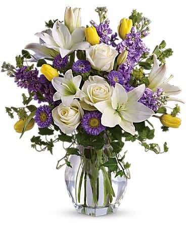Spring Waltz - Graceful, elegant and timeless, this beautiful spring bouquet offers up colors, blossoms and textures in perfect harmony. Serene crÃ¨me roses, yellow tulips, white asiatic lilies, lavender stock and matsumoto asters are perfectly arranged with spring's freshest greenery and delivered in a lovely clear glass vase. Send it and you'll definitely waltz right in to someone's good graces!