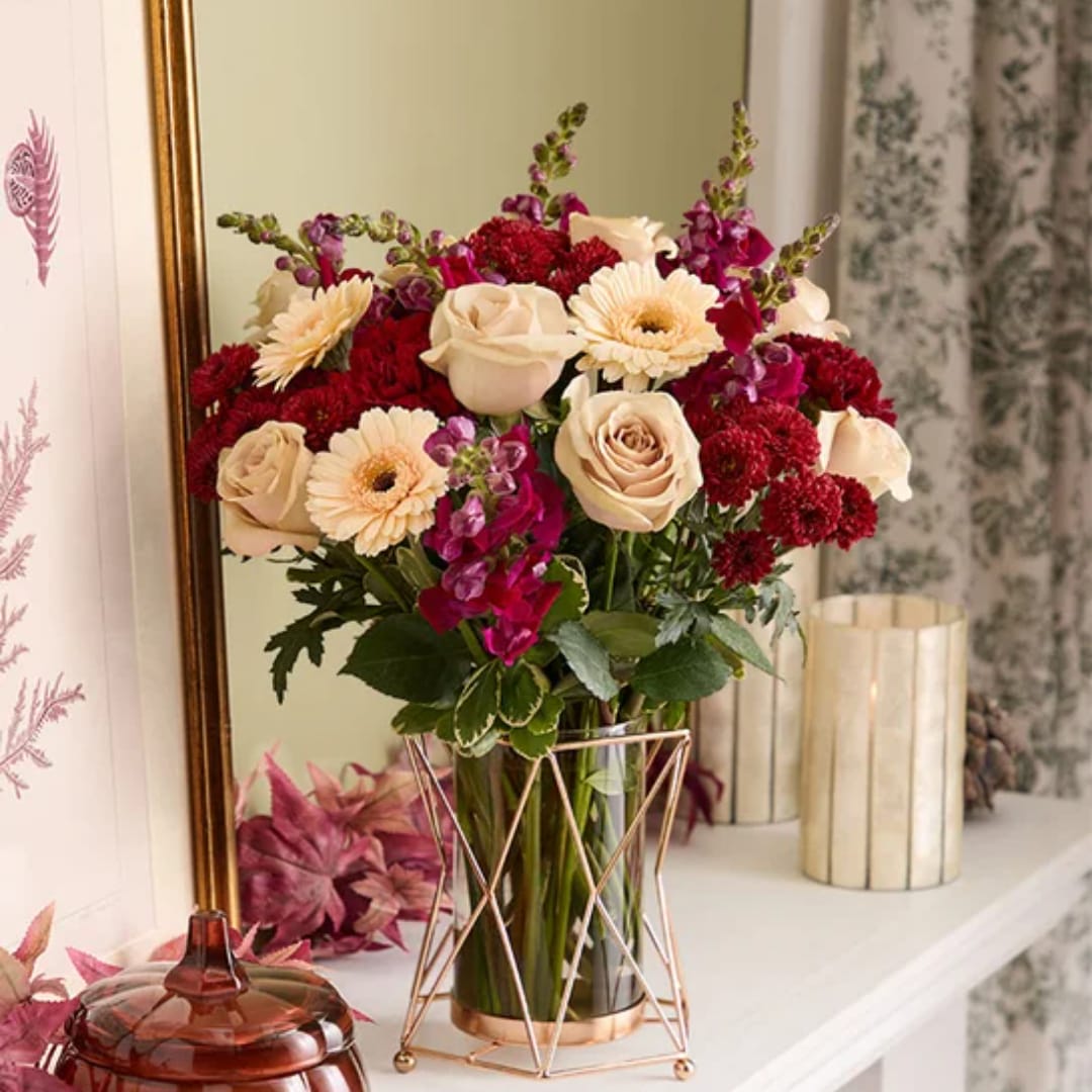 Bouquet of cream roses, red mums, and purple flowers in a glass vase