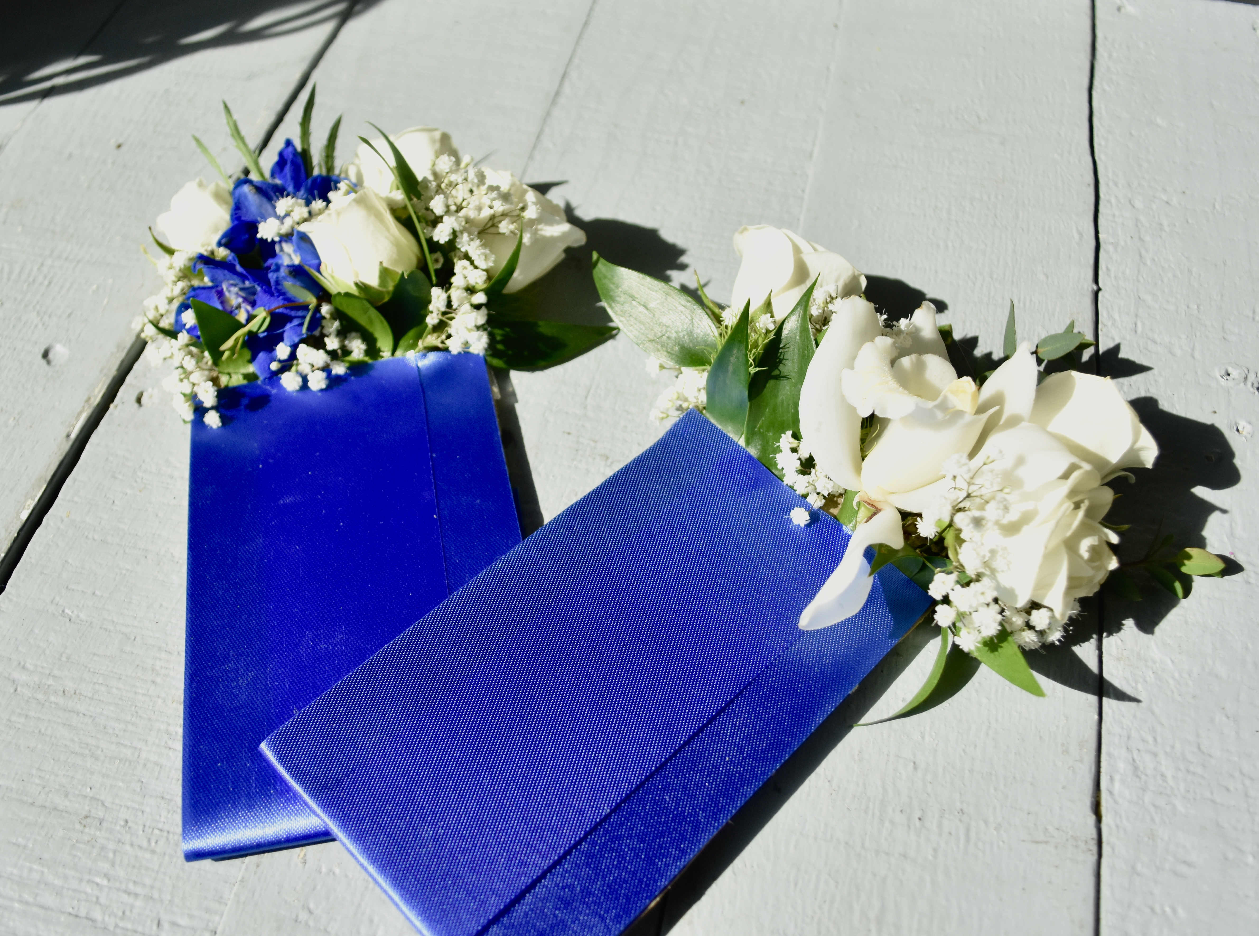 Two blue ribbon corsages with white flowers on a light surface