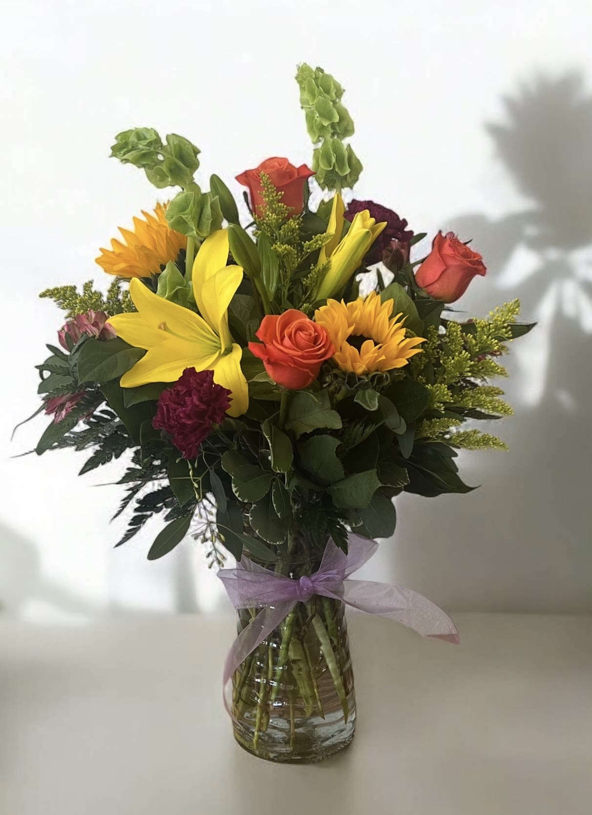 Mixed bouquet of lilies, roses, and sunflowers in a glass vase