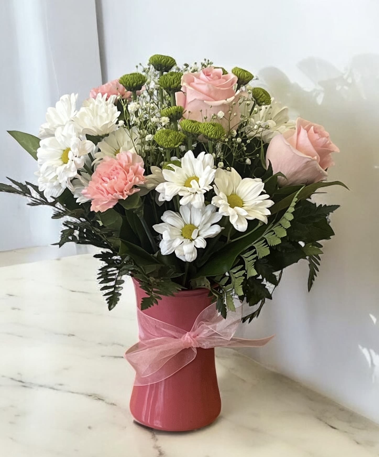 Pink roses and white daisies in a pink vase with a ribbon