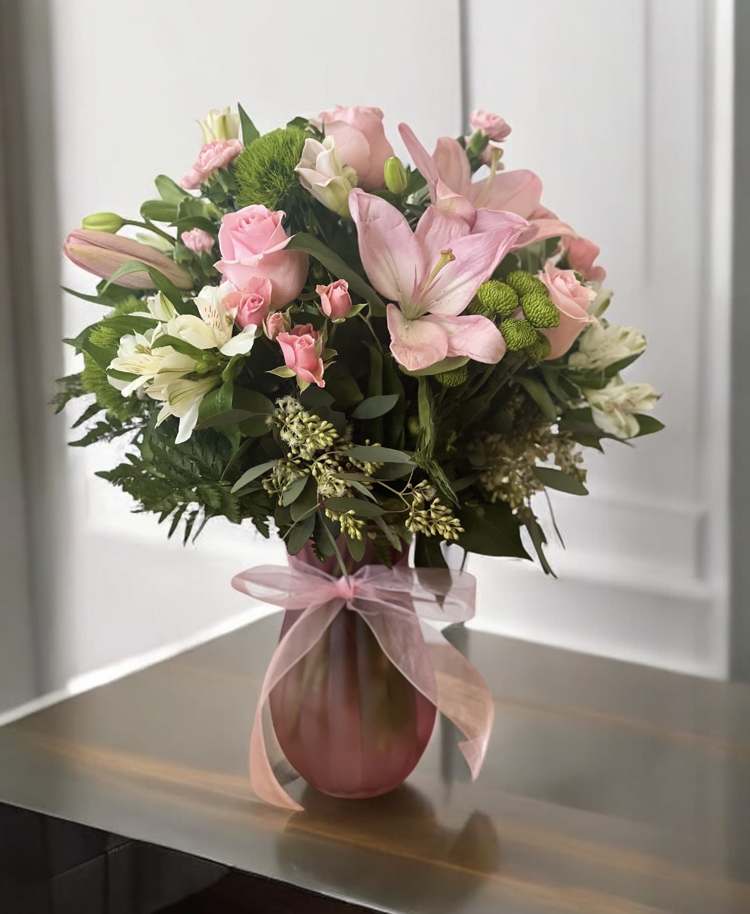 Pink and white mixed flower bouquet in a pink vase with ribbon