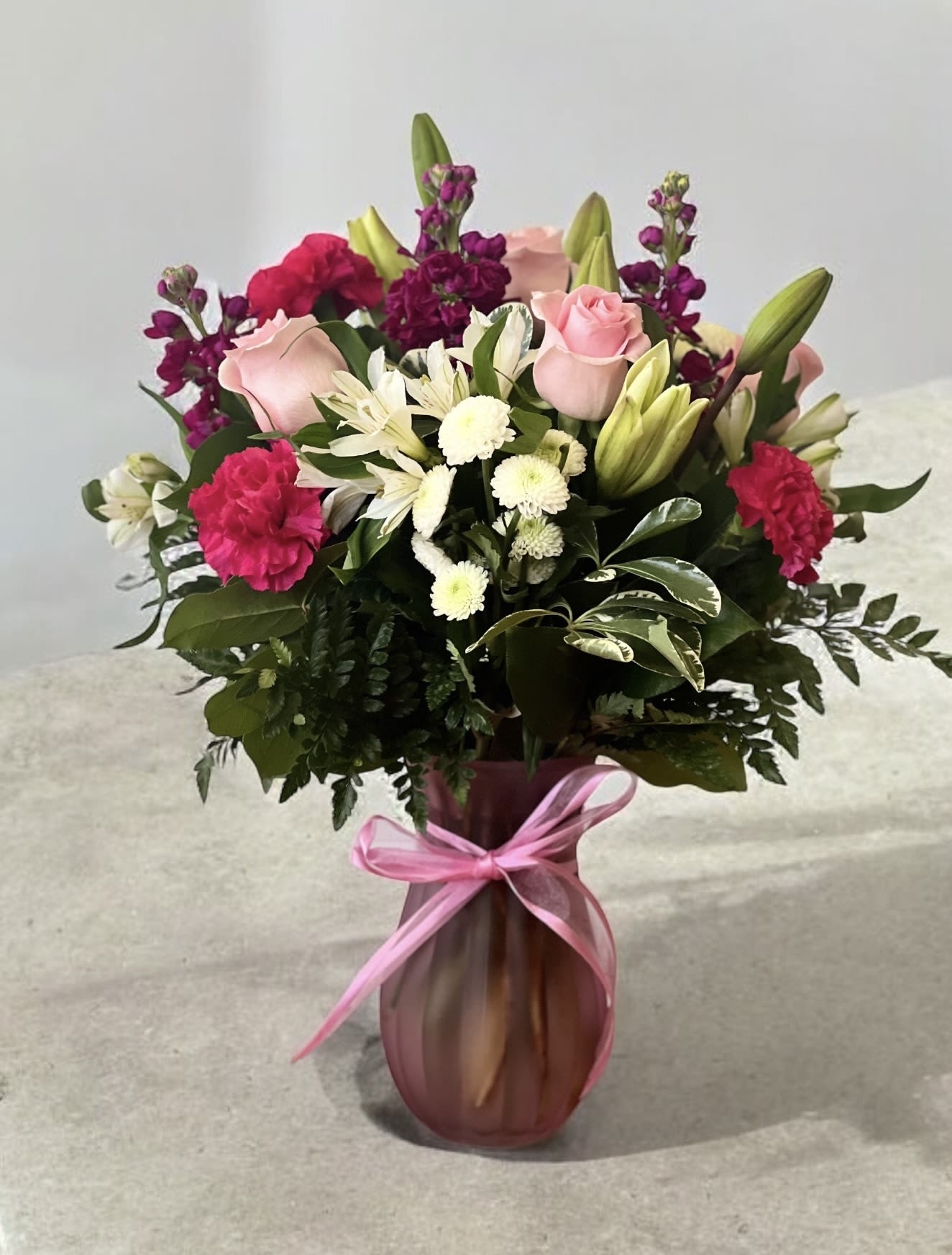 Pink roses and mixed flowers arranged in a vase with a ribbon