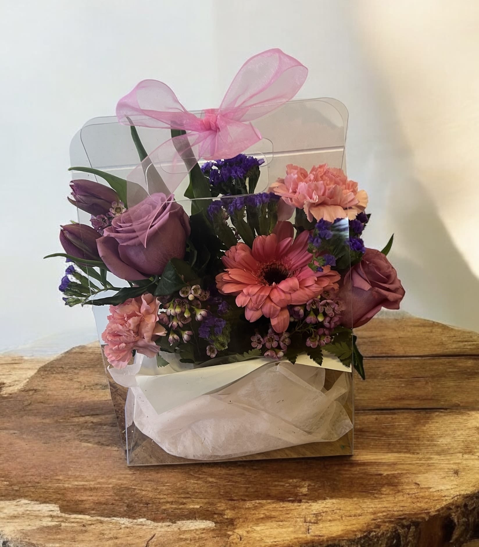 Pink and purple flower arrangement in a clear gift box with a ribbon