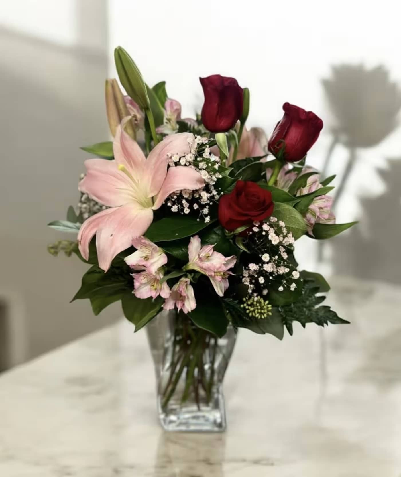Bouquet of pink lilies and red roses in a clear glass vase
