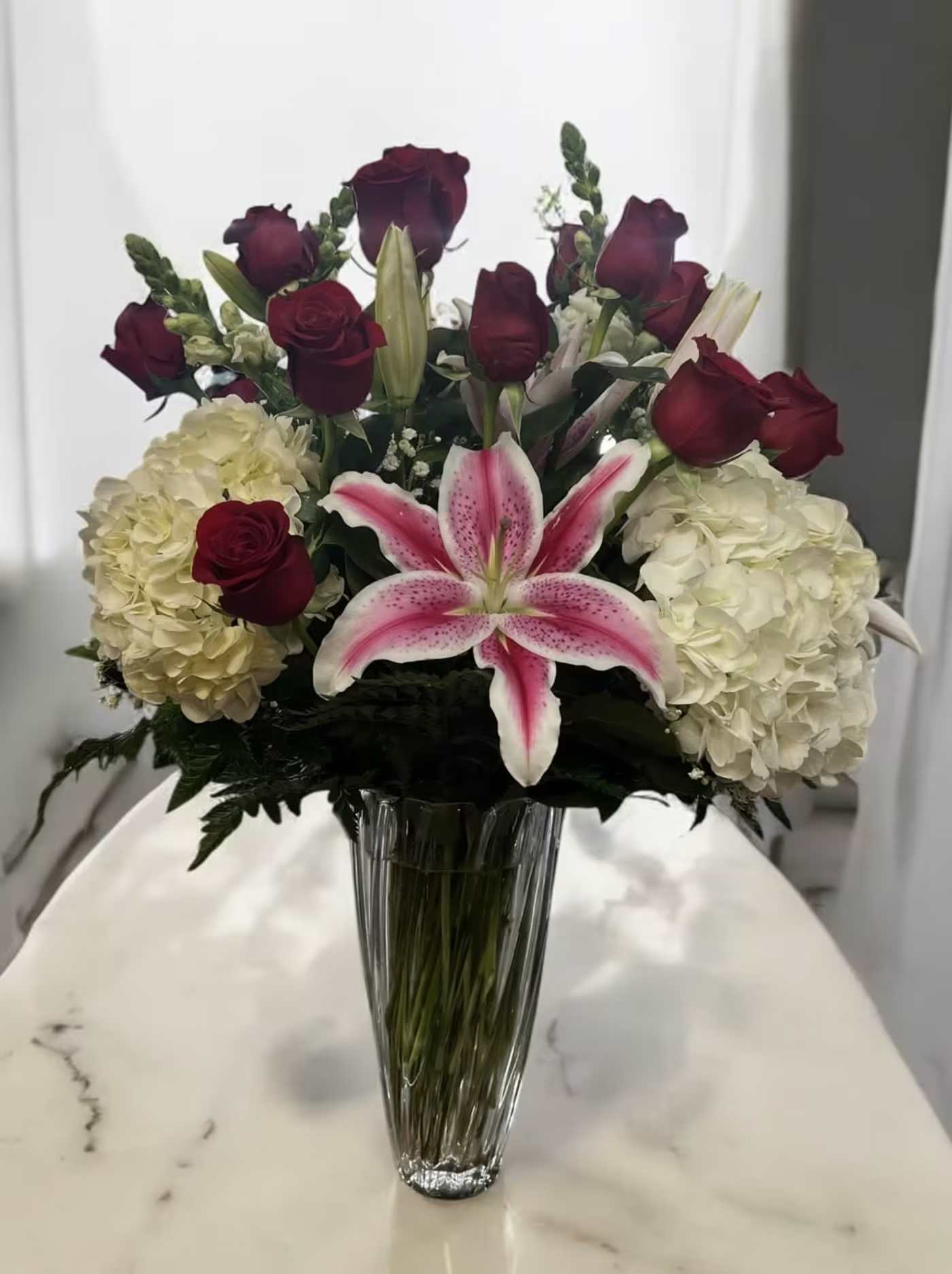 Bouquet of red roses, white hydrangeas, and a pink lily in a glass vase