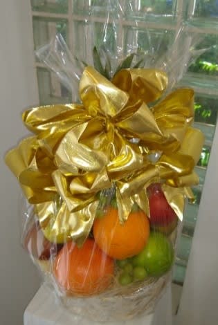 Gift basket of assorted fresh fruit wrapped in cellophane with a large gold bow