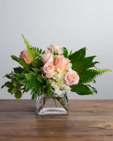 Peaches - Peaches captures the essence of the garden with flowers like soft peach roses and white hydrangea nestled in lush foliage in a cube vase.
