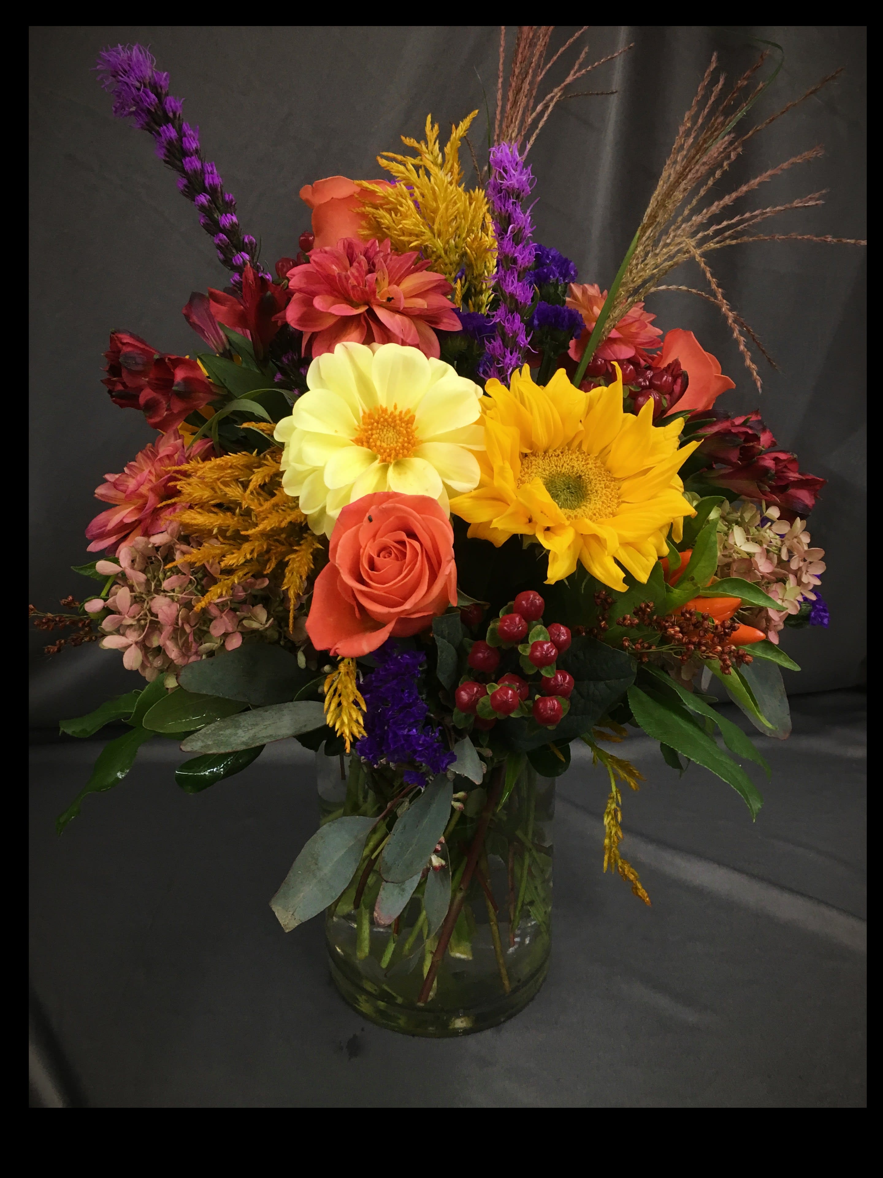 Fall Abundance - A bright, colorful mix of fall seasonal flowers arranged in a sleek cylinder vase. Dahlias, Sunflowers, and stunning orange roses make this arrangement a real show stopper!  *Pictured at Delux Pricing*