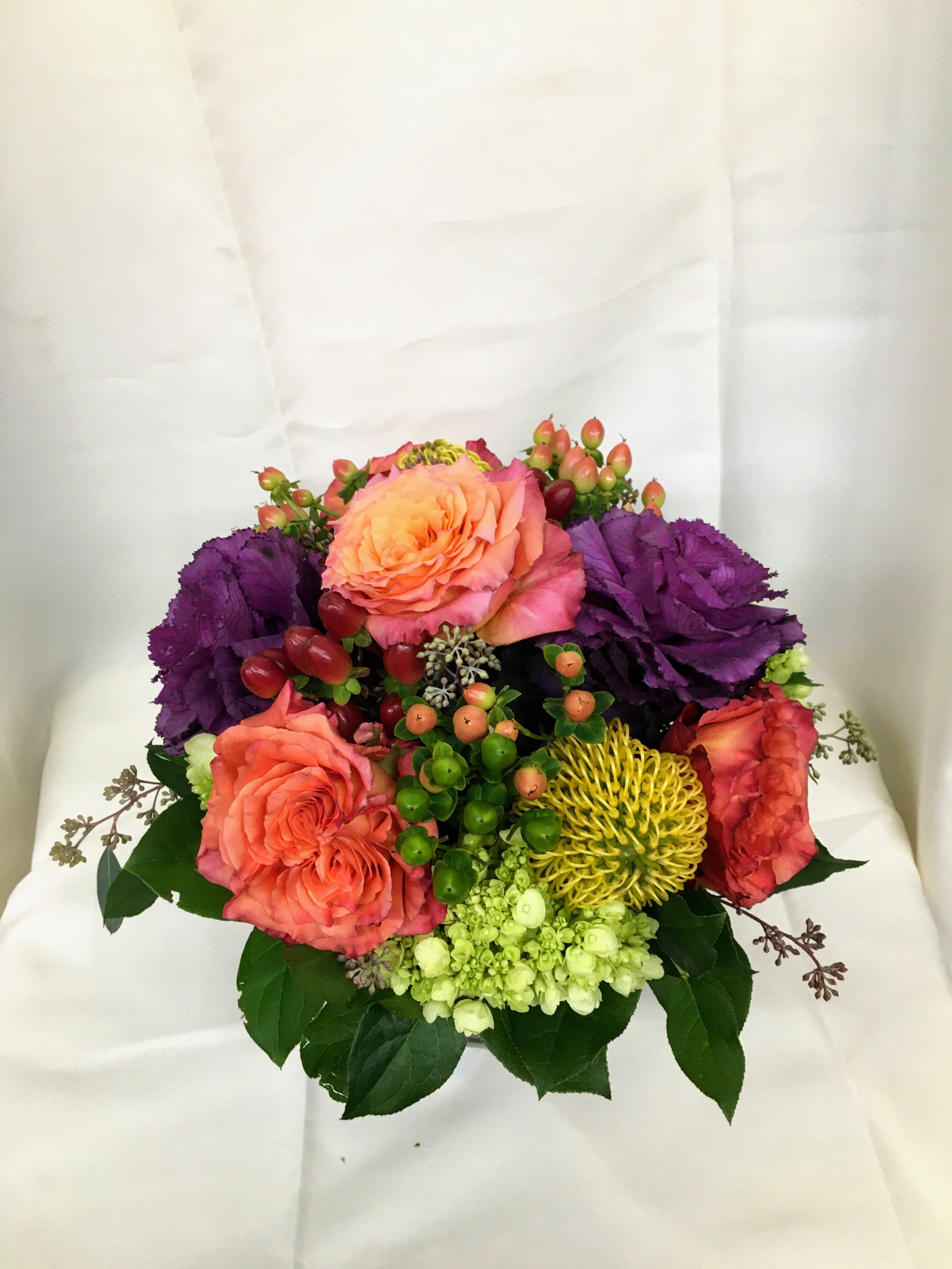 Autumn Abundance - A mixture of fall colored roses, kale, pincushion protea, with accents of hypericum, and seeded eucalyptus arranged in a glass cube. A beautiful mixture of flowers that is reminiscent of fall.