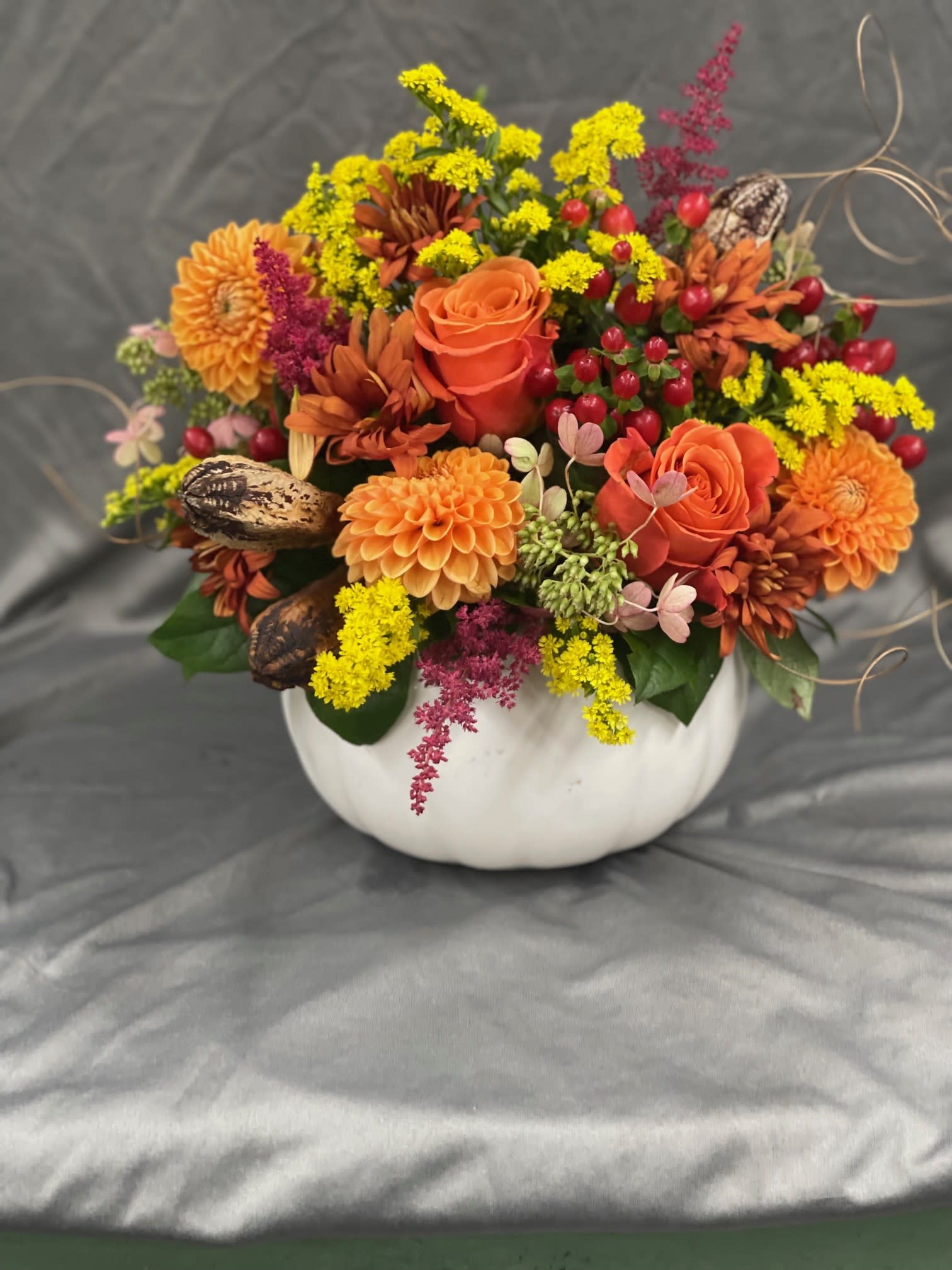 Orange and yellow floral arrangement in a white pumpkin-shaped container