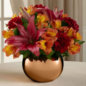 Bouquet of red, orange, and yellow flowers in a copper vase