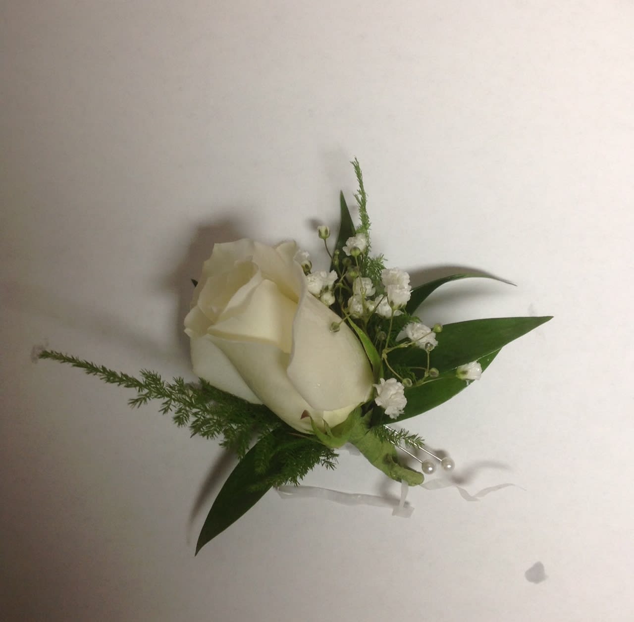 White rose boutonniere with baby's breath and green leaves