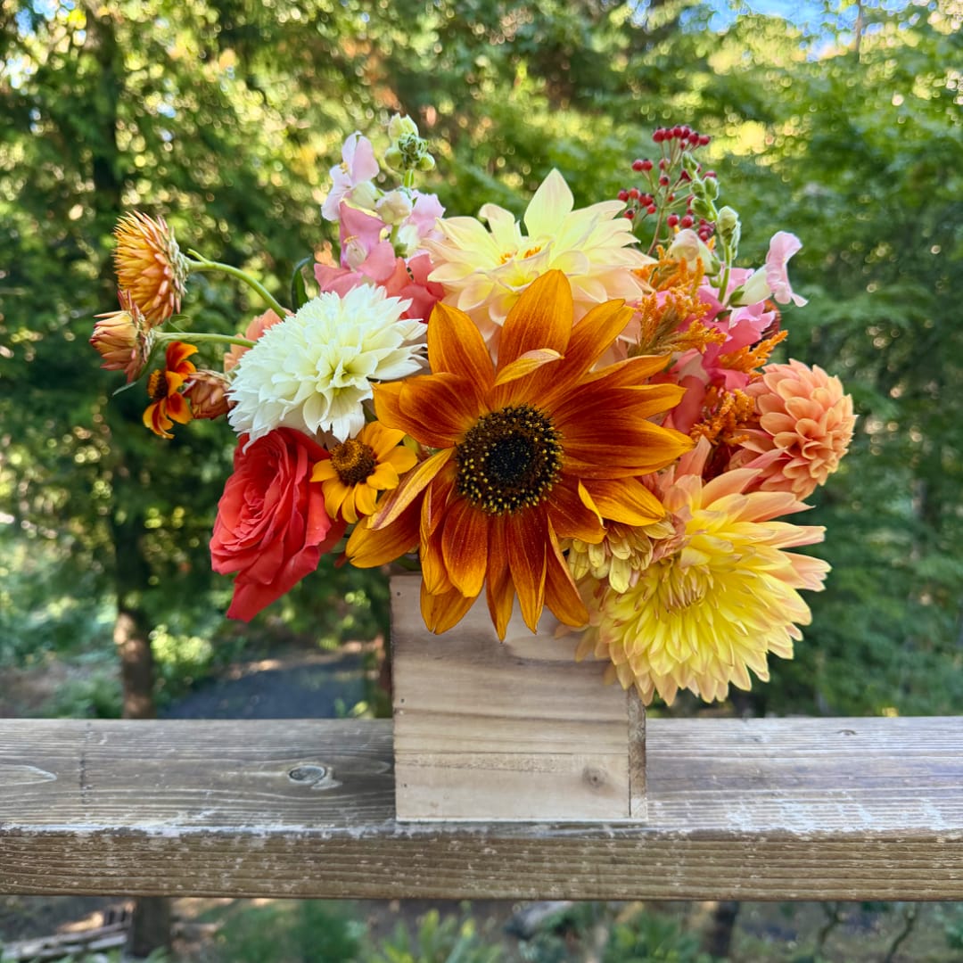 Mixed bouquet of orange, yellow, pink, and white flowers in a wooden box