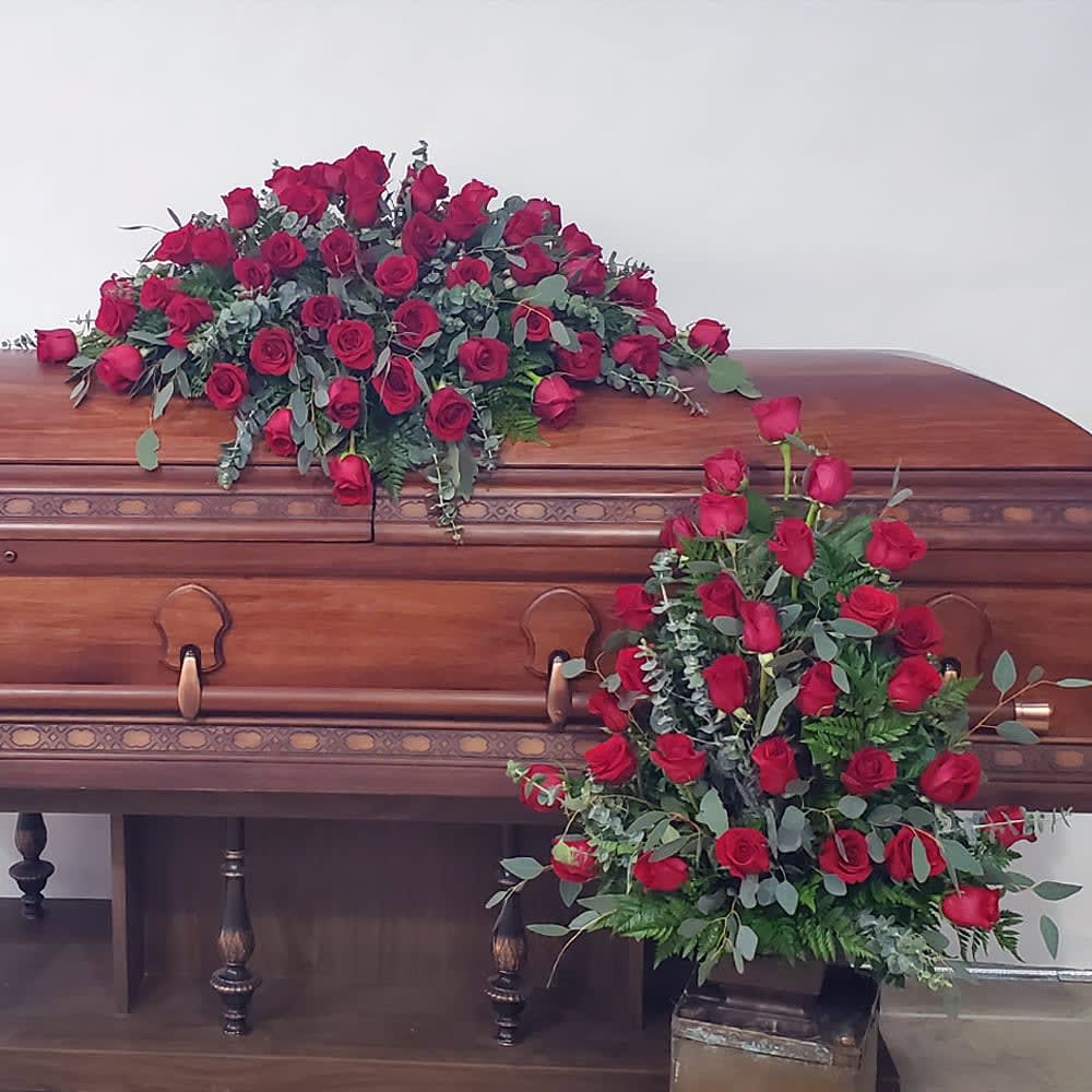 Red rose casket spray and standing floral arrangement on a wooden casket