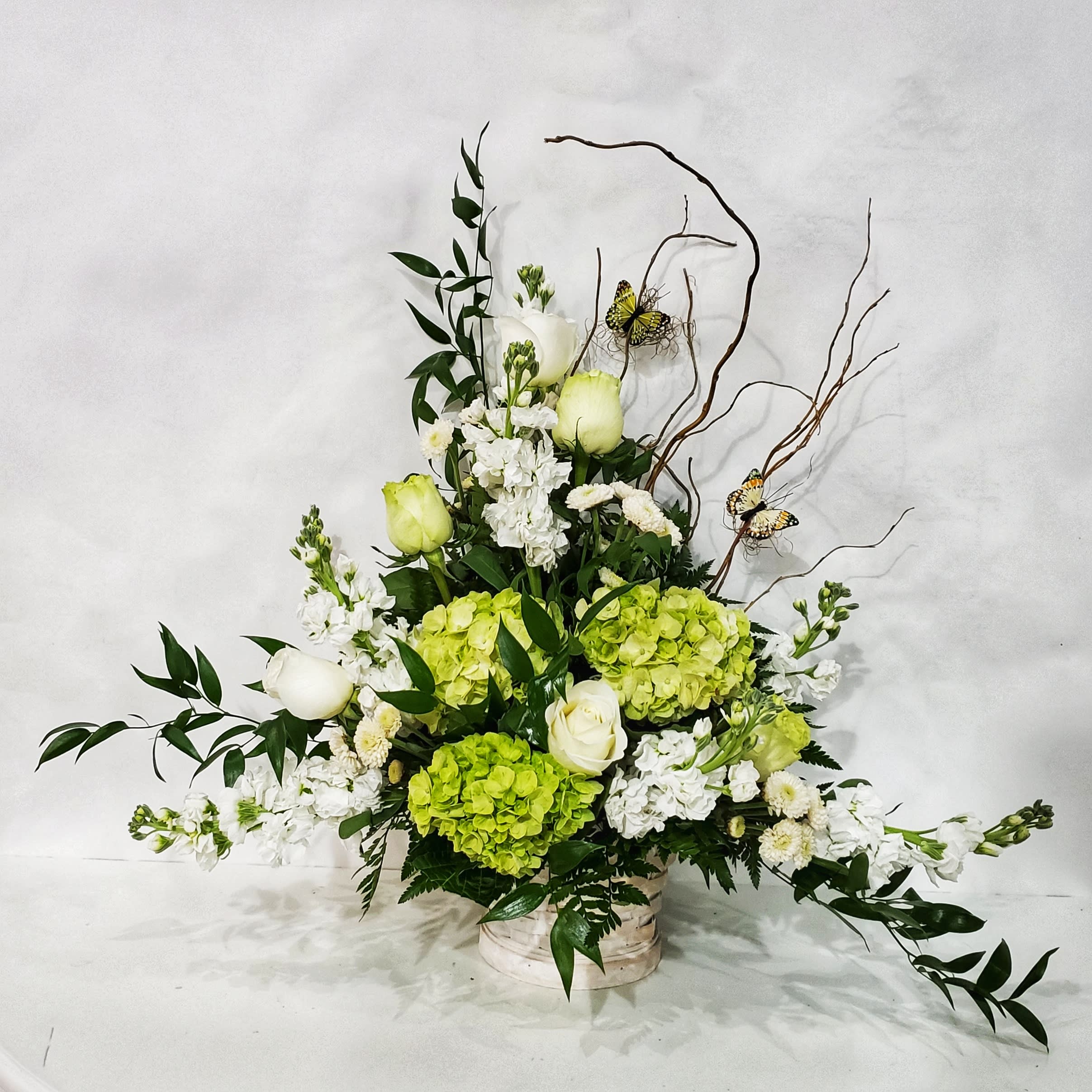 Tall floral arrangement with white roses, green hydrangeas, and butterflies in a low container