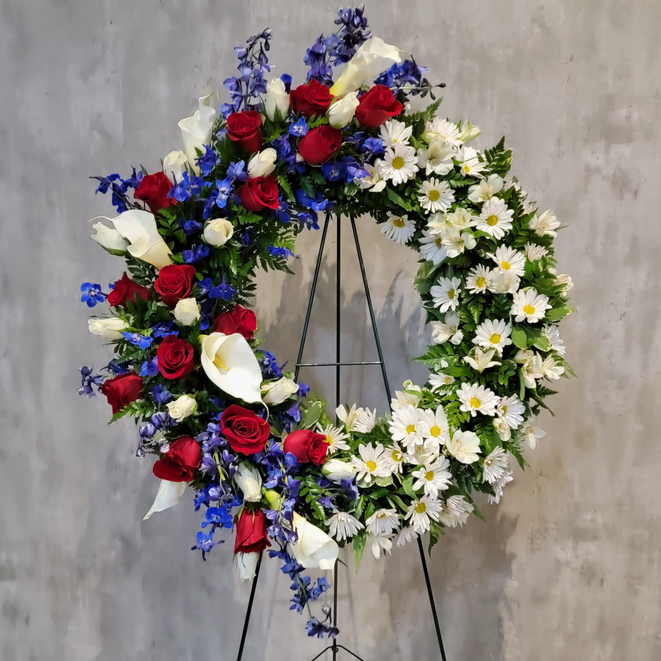 Large floral wreath with red roses, white calla lilies, and white daisies on a stand