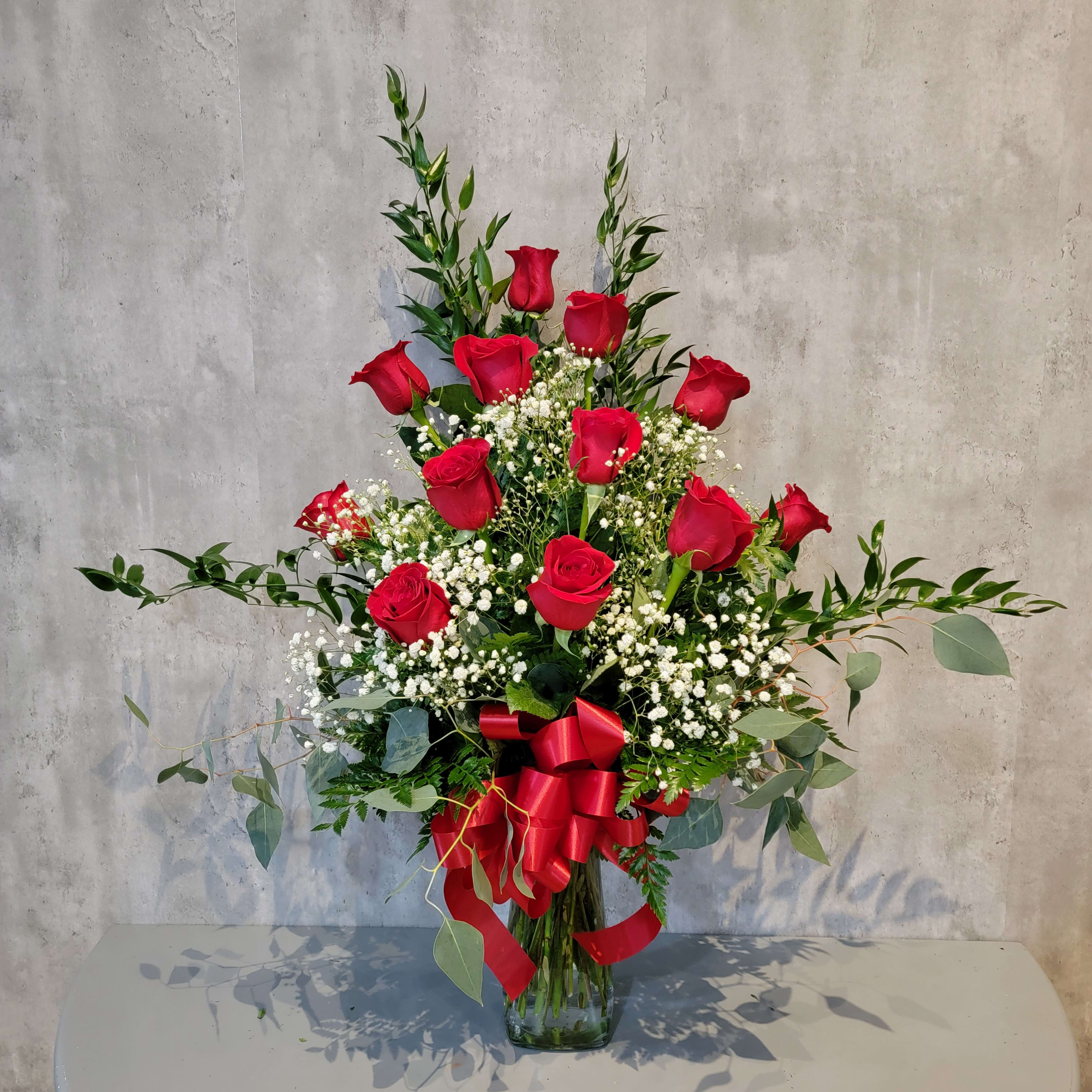 Red roses arranged in a clear glass vase with baby's breath and greenery