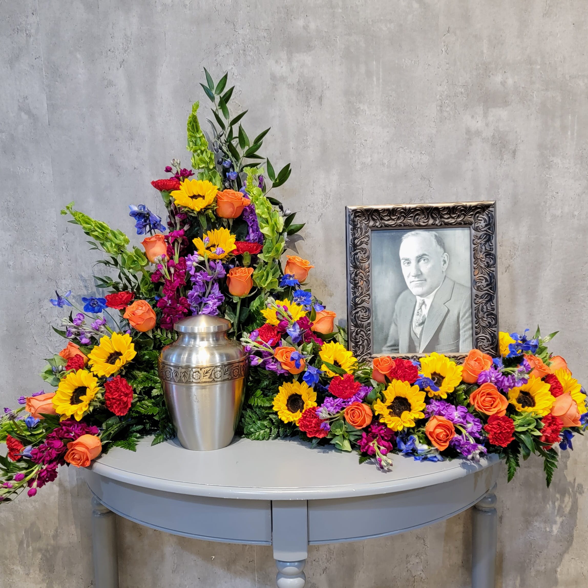Colorful floral funeral tribute with a framed portrait and silver urn