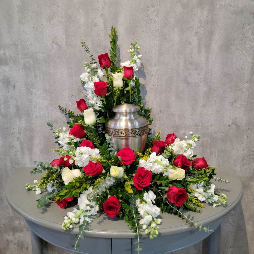 Red and white roses arranged around a silver urn on a table