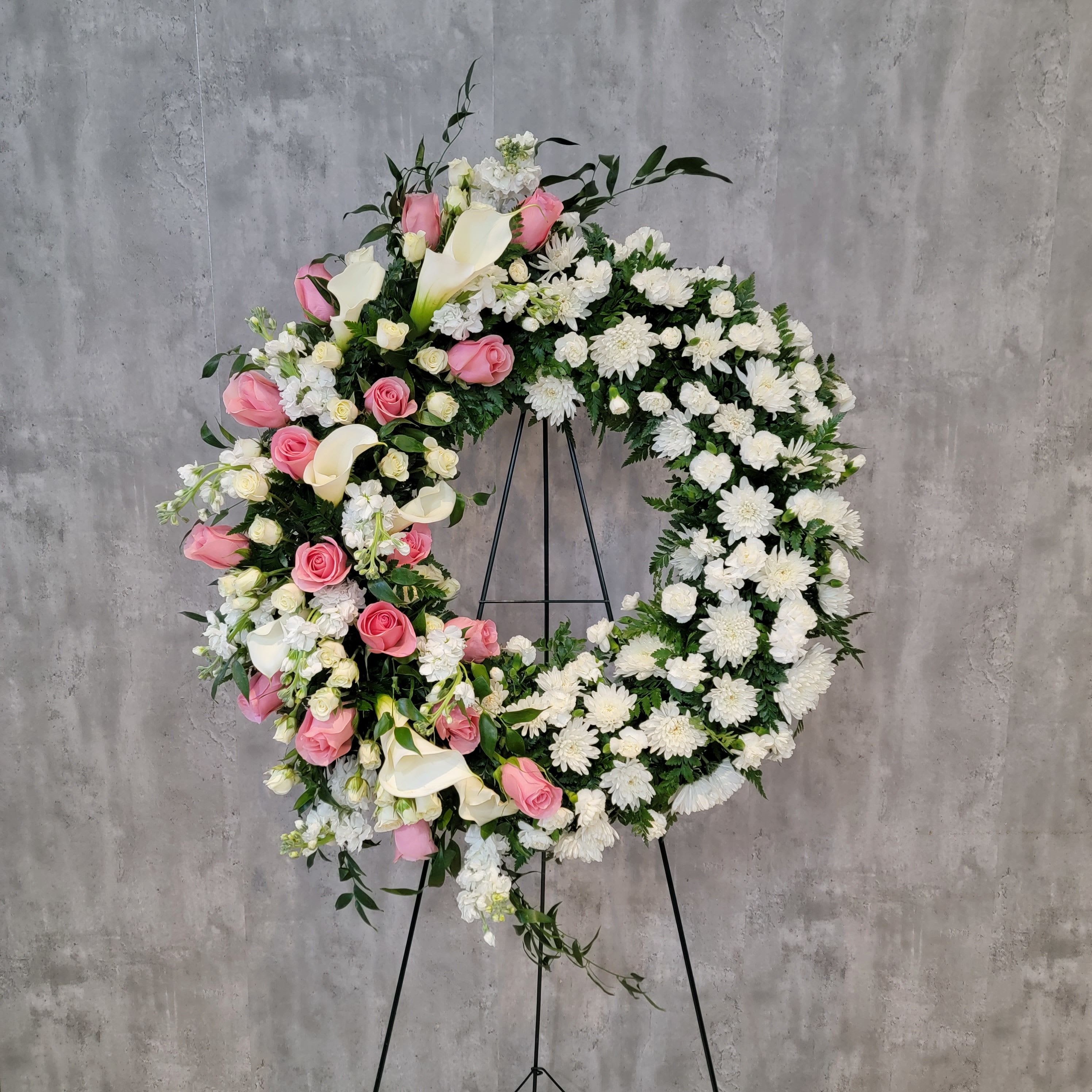Large floral wreath with pink and white flowers on a black stand
