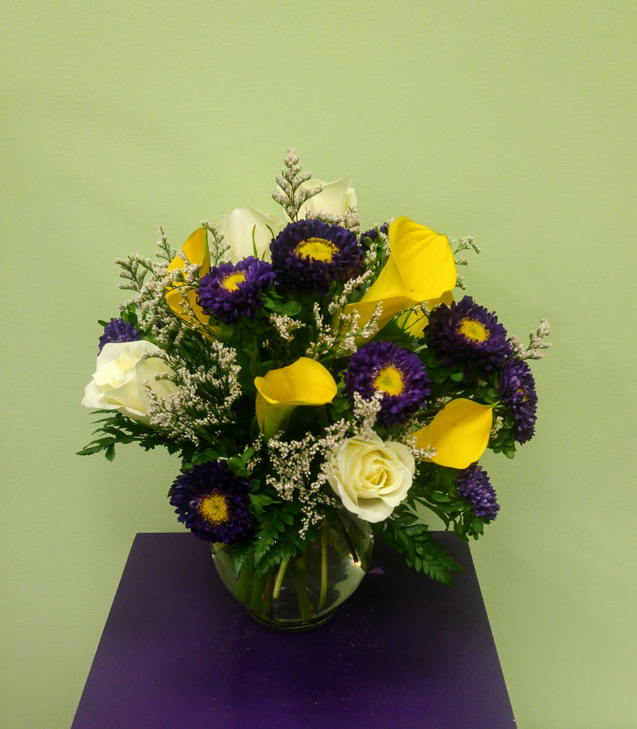 Bouquet of purple daisies, yellow calla lilies, and white roses in a glass vase