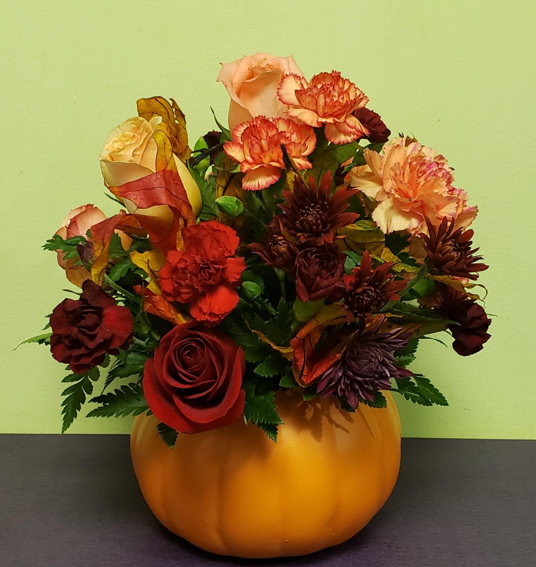 Autumn floral arrangement in a pumpkin-shaped container with roses and carnations
