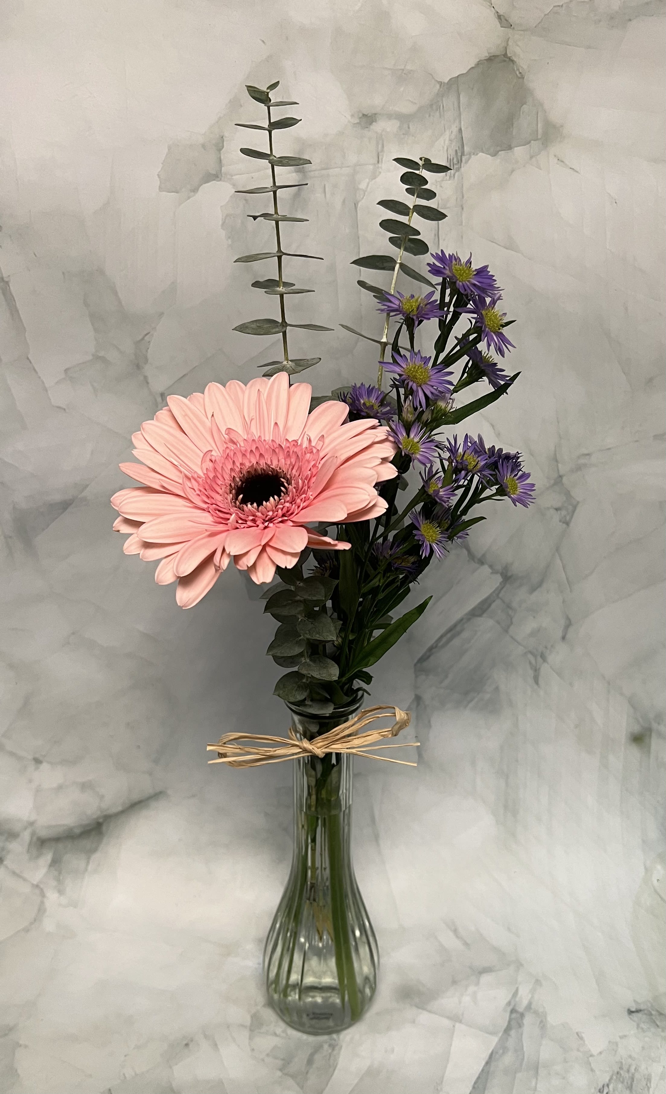 Pink gerbera daisy and purple asters in a glass vase with a bow.