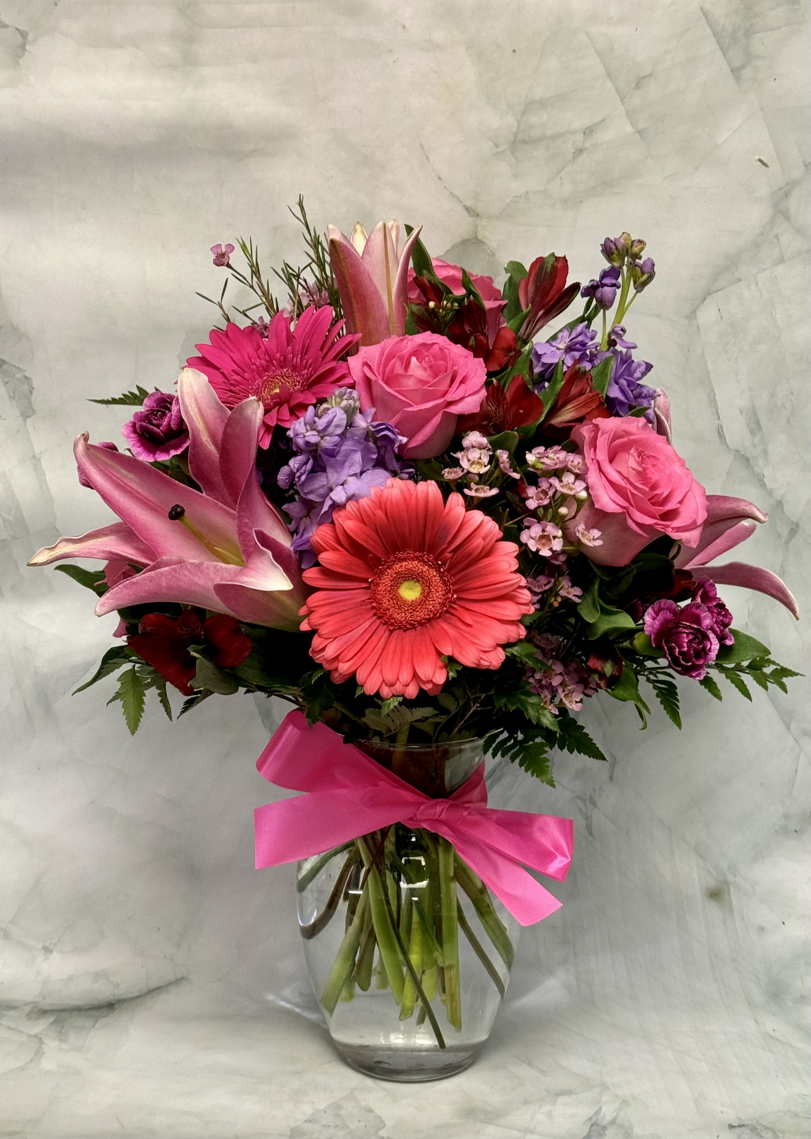 Pink and purple mixed bouquet in a glass vase with a bright ribbon