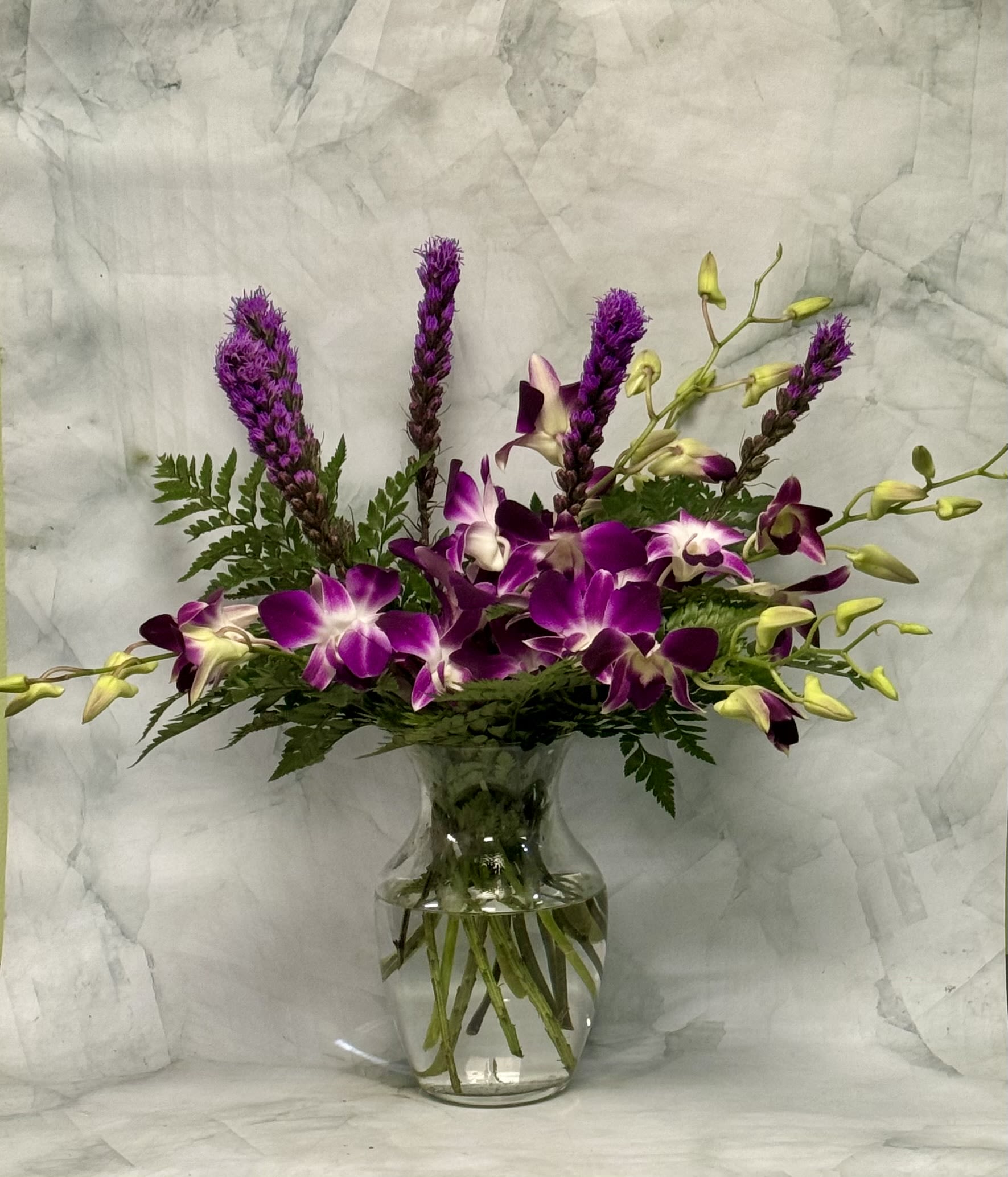 Purple orchids and tall purple spikes in a clear glass vase
