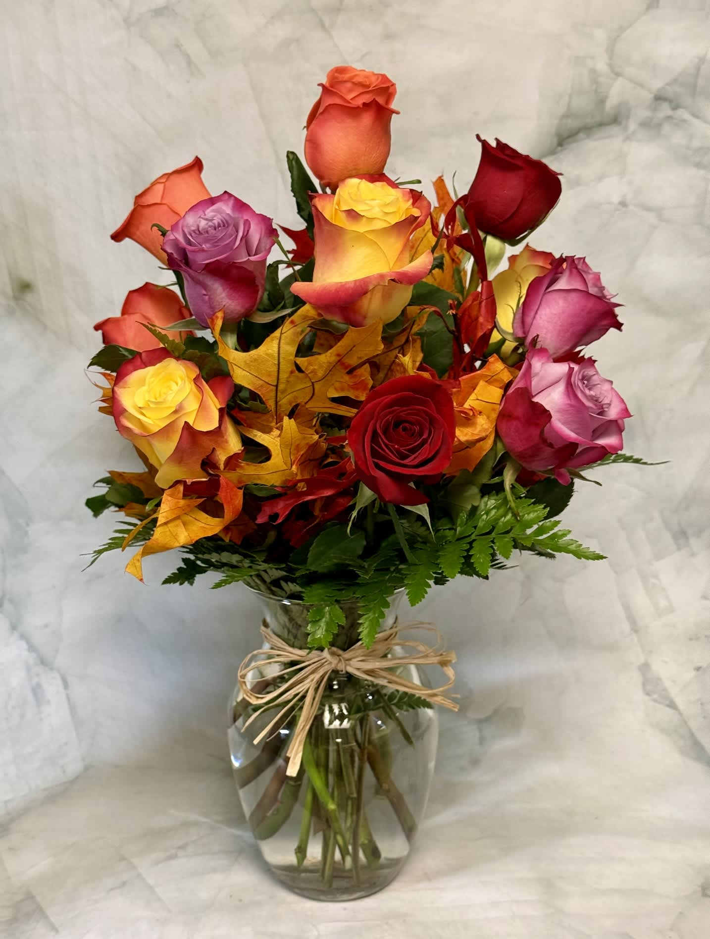 Mixed roses in a glass vase with autumn leaves
