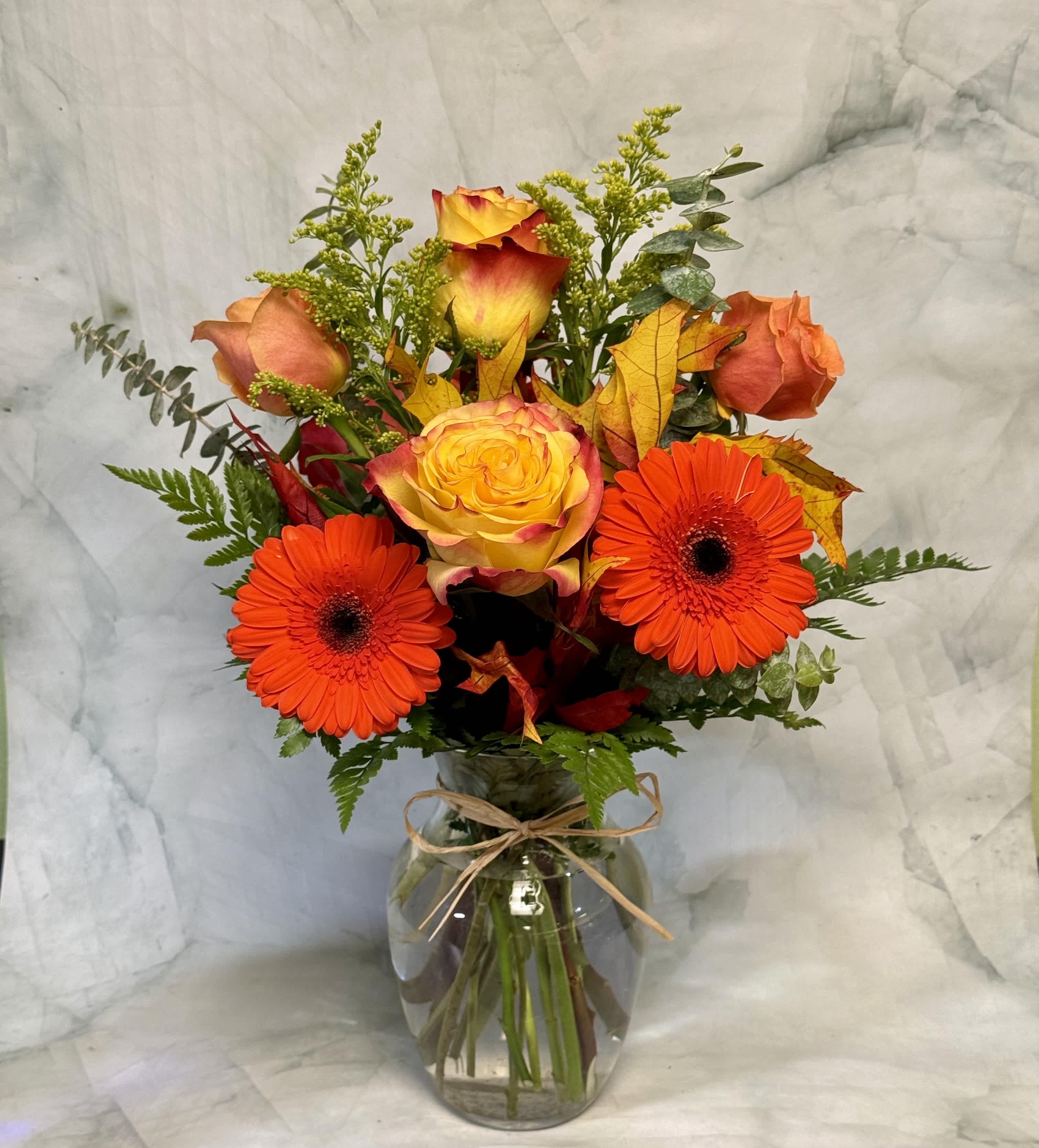 Bouquet of orange gerbera daisies and yellow-orange roses in a glass vase