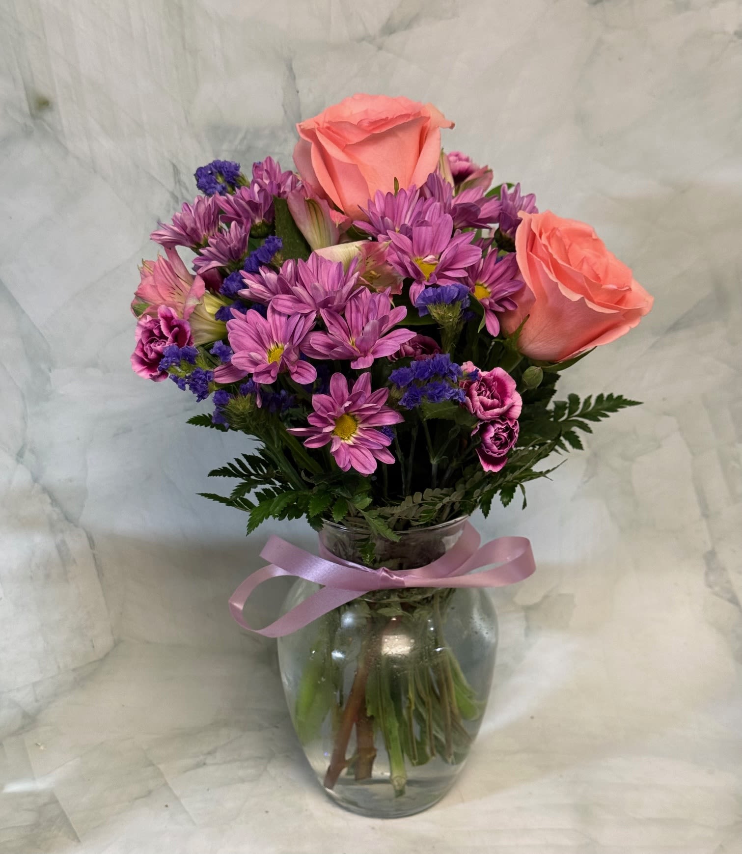 Pink roses and purple daisies in a glass vase with a ribbon
