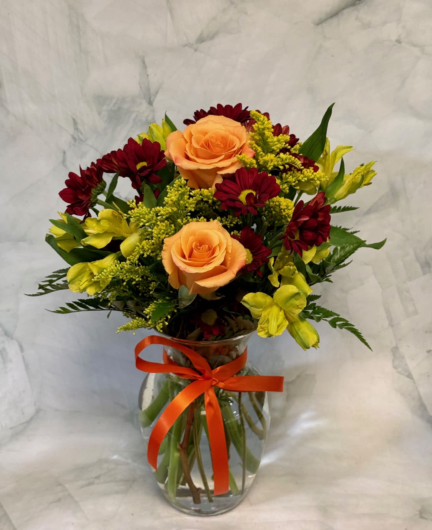 Bouquet of peach roses, red daisies, and yellow flowers in a glass vase