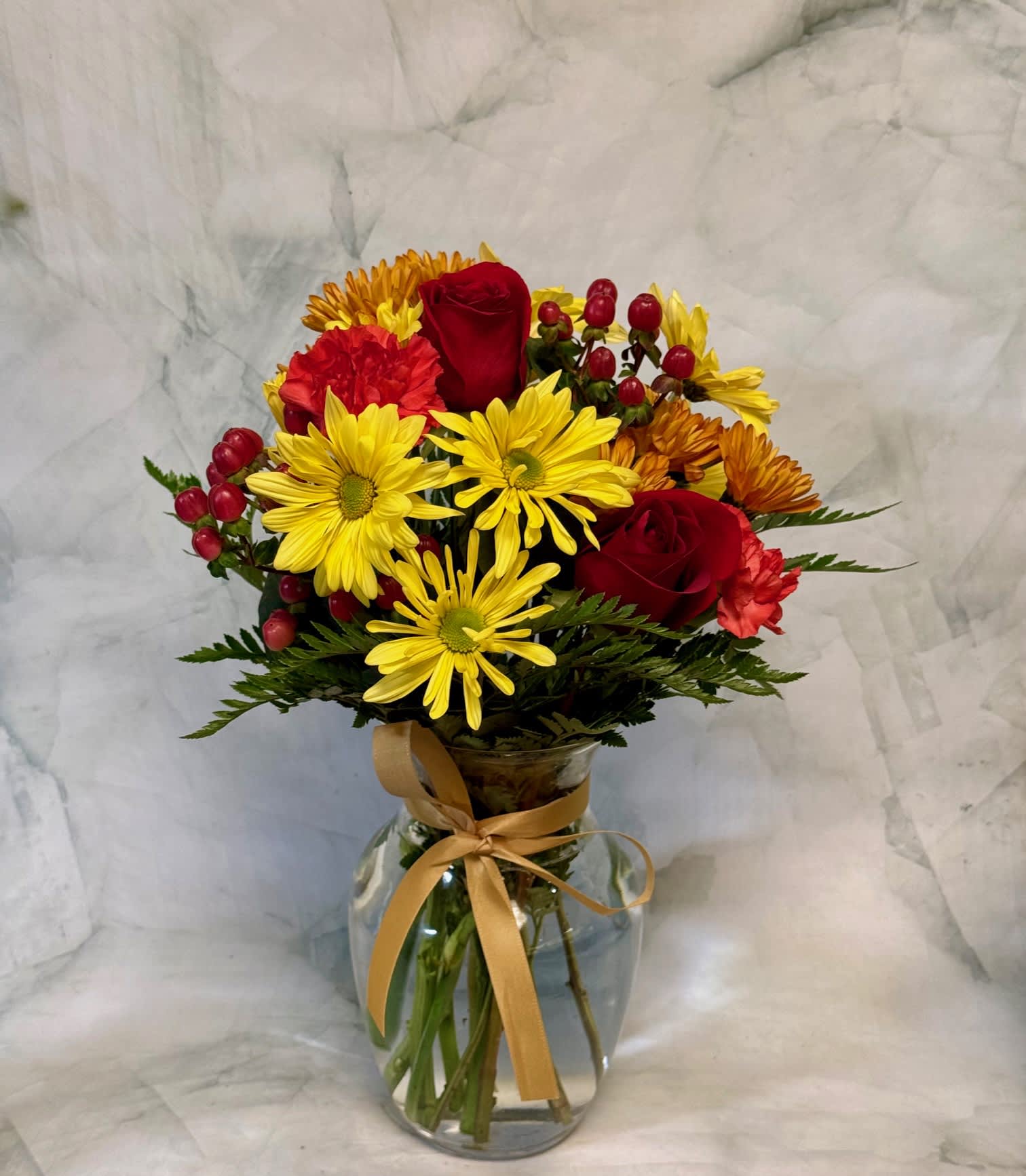 Bouquet of red roses and yellow daisies in a glass vase with a ribbon