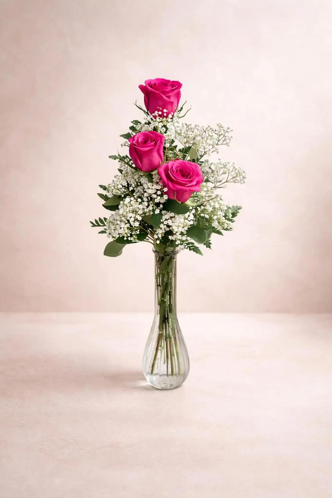 Three pink roses in a clear glass vase with white filler flowers