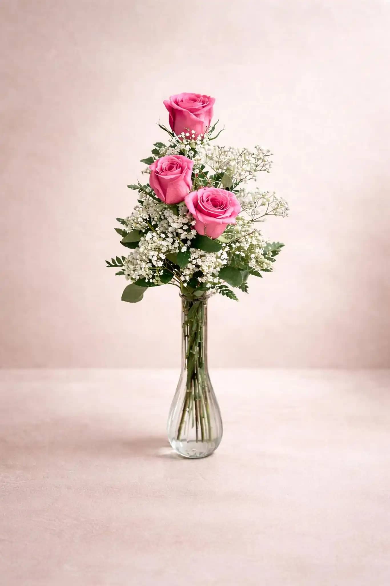 Three pink roses arranged in a clear glass vase with white filler flowers.