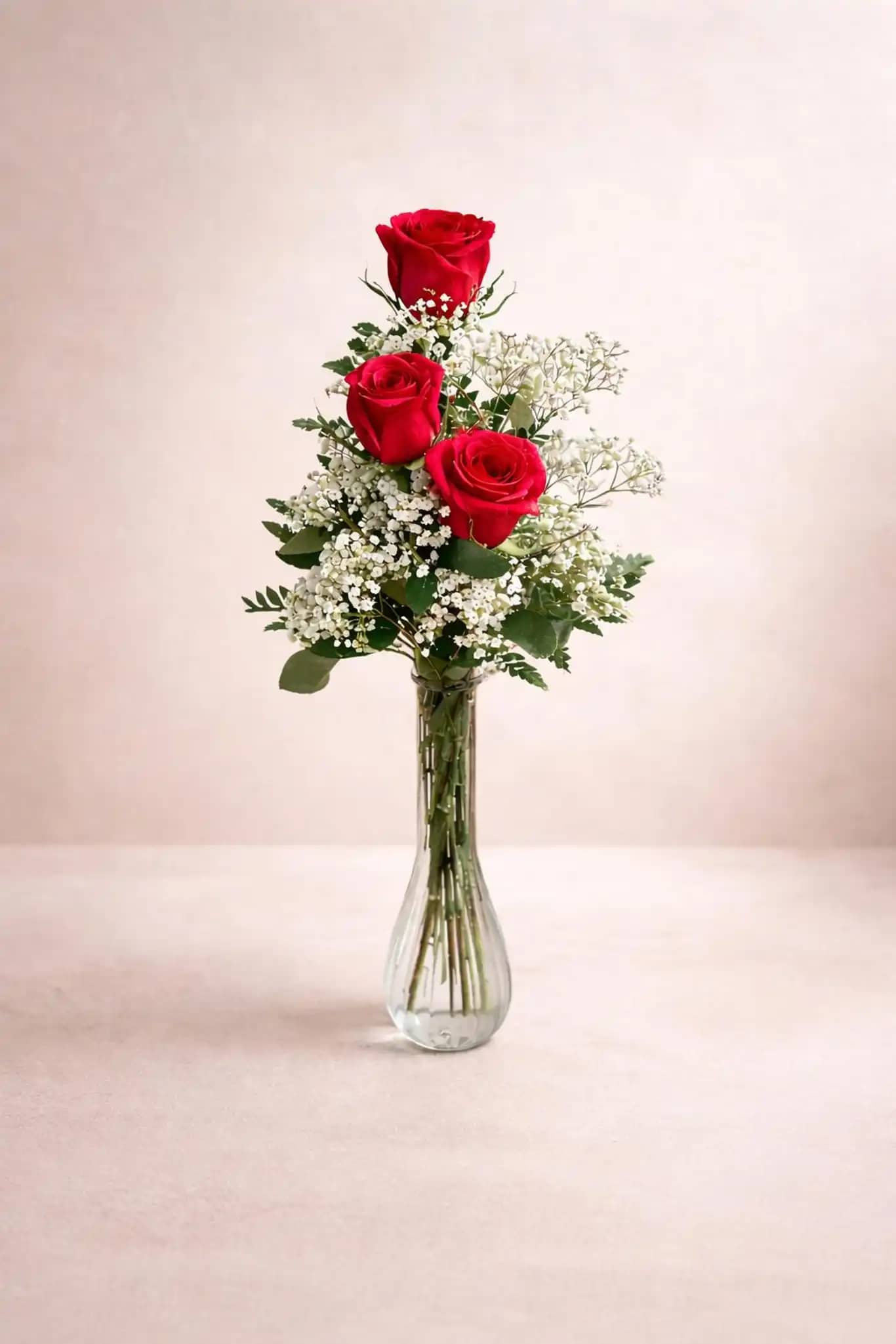 Three red roses arranged in a clear glass vase with white filler flowers