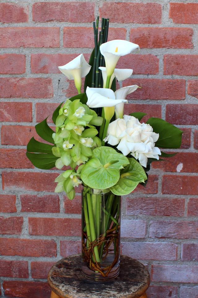 White calla lilies and green orchids in a tall glass vase