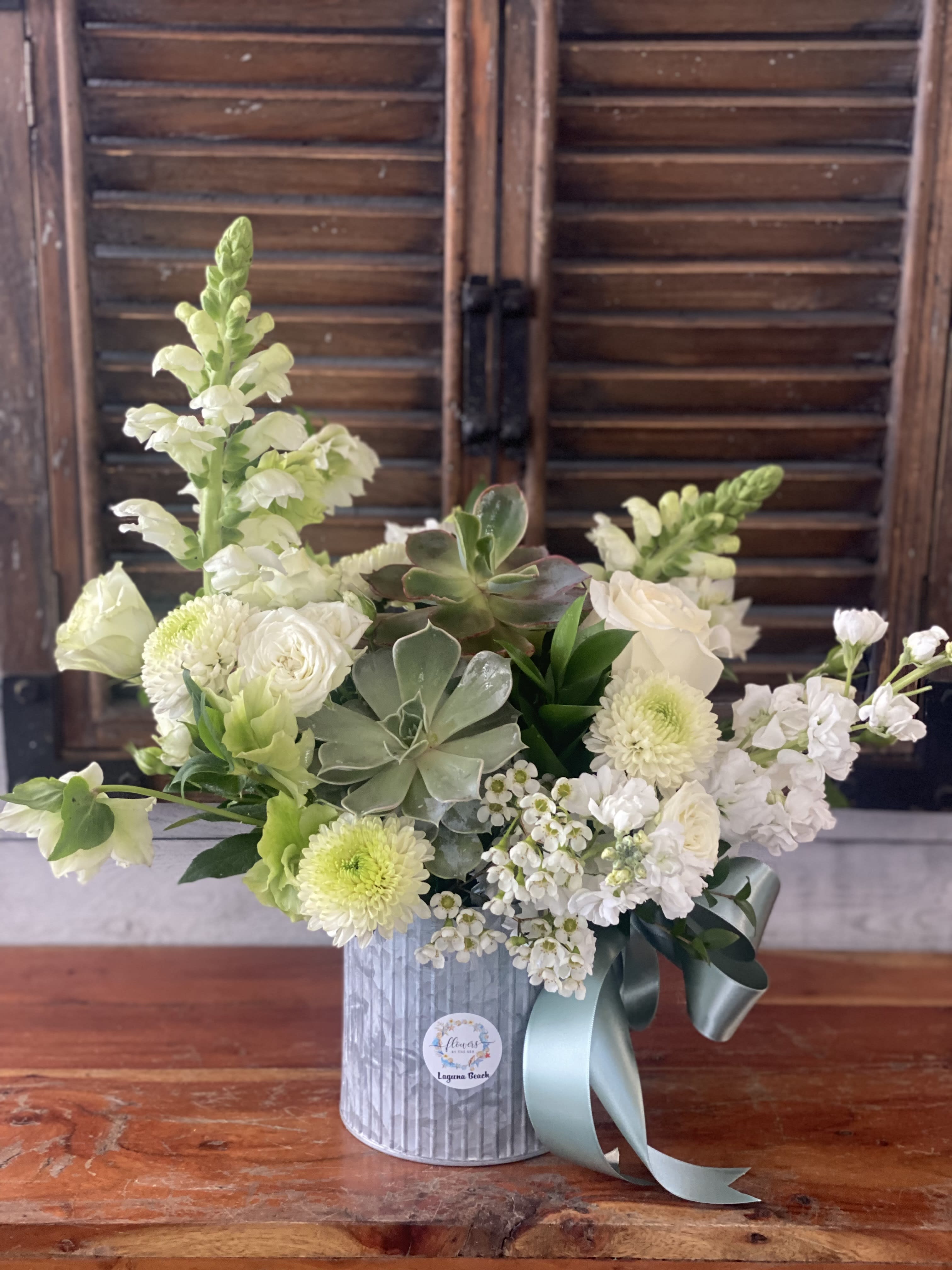 White floral arrangement in a silver tin with a blue ribbon
