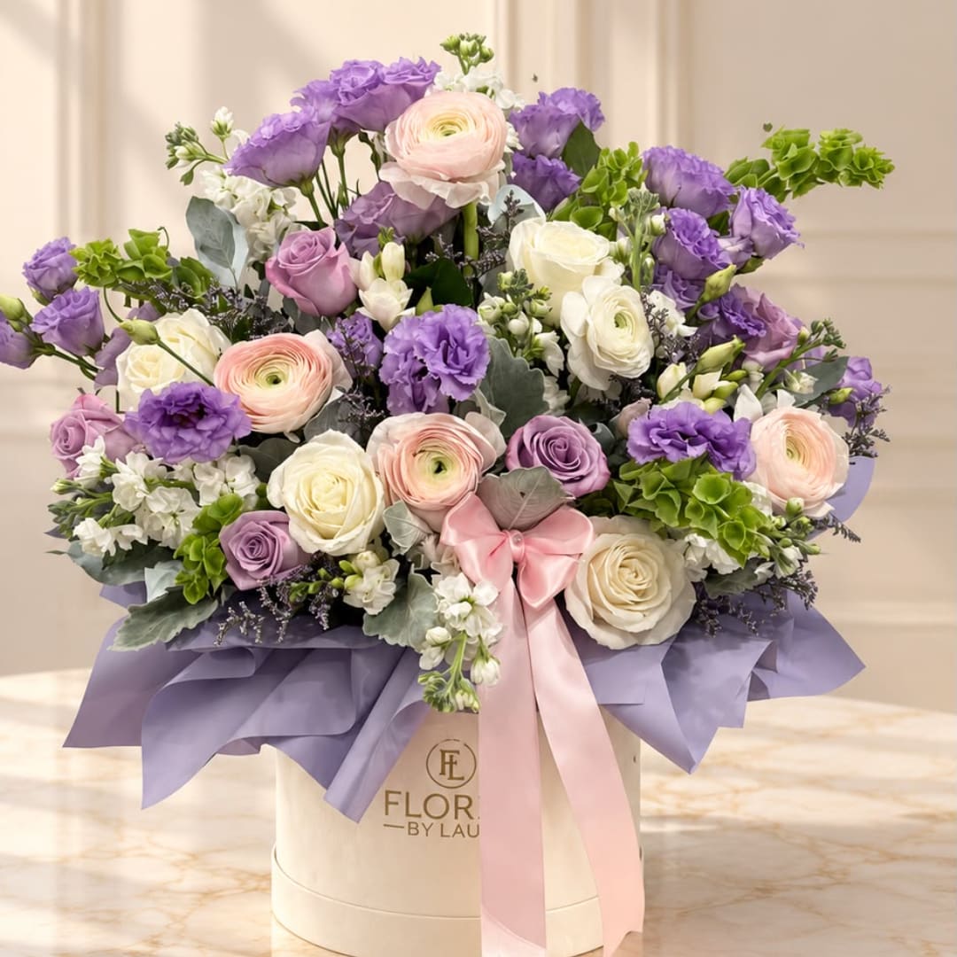 Lavender and blush floral arrangement in a cream hat box with a pink ribbon