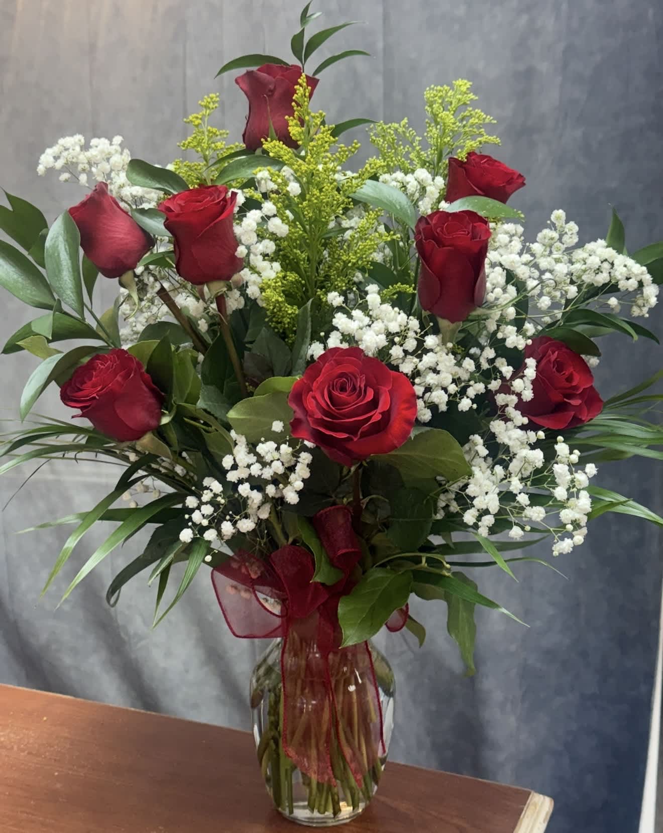 Red roses and white baby's breath in a clear glass vase with a red ribbon