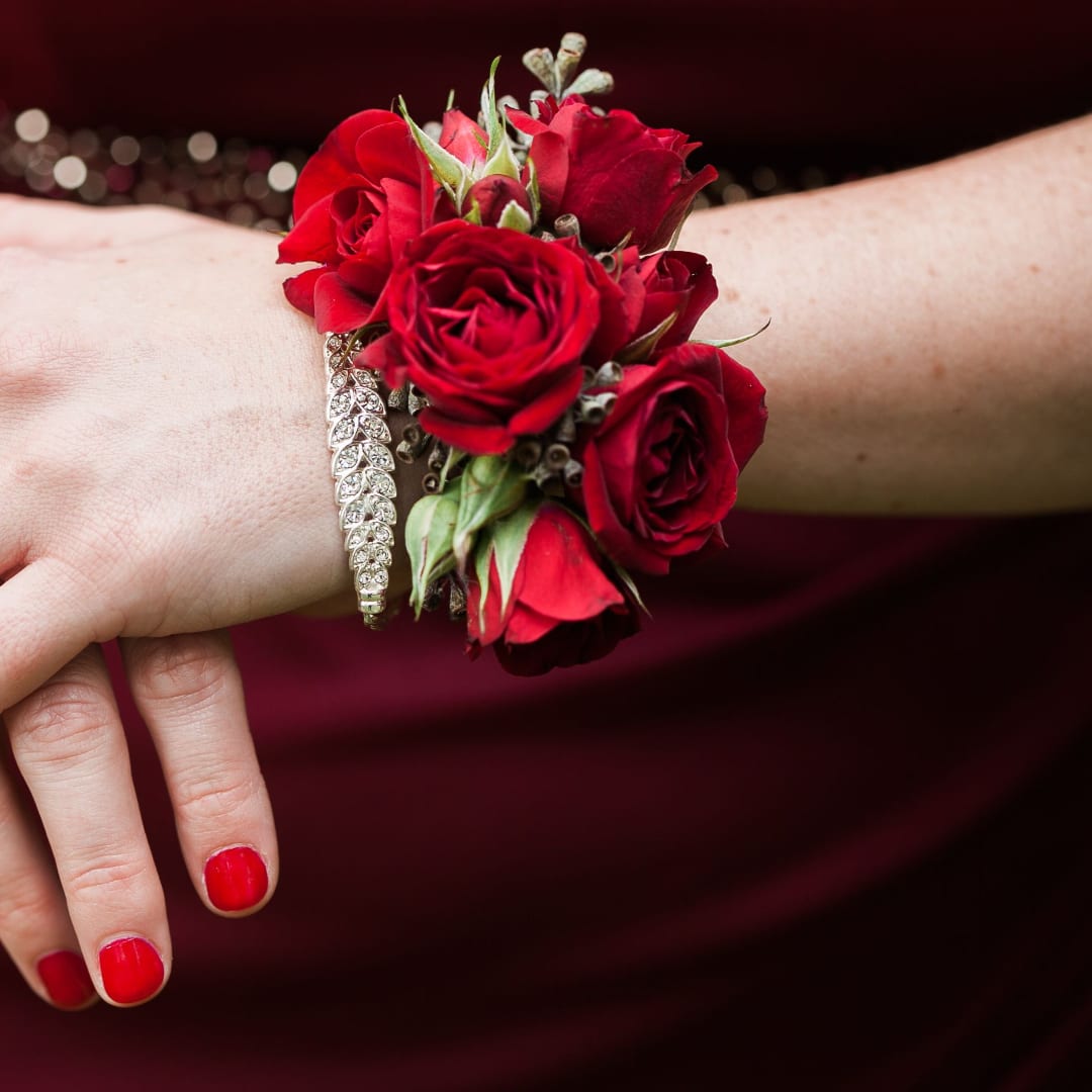 Red rose wrist corsage with a jeweled bracelet on a person's wrist