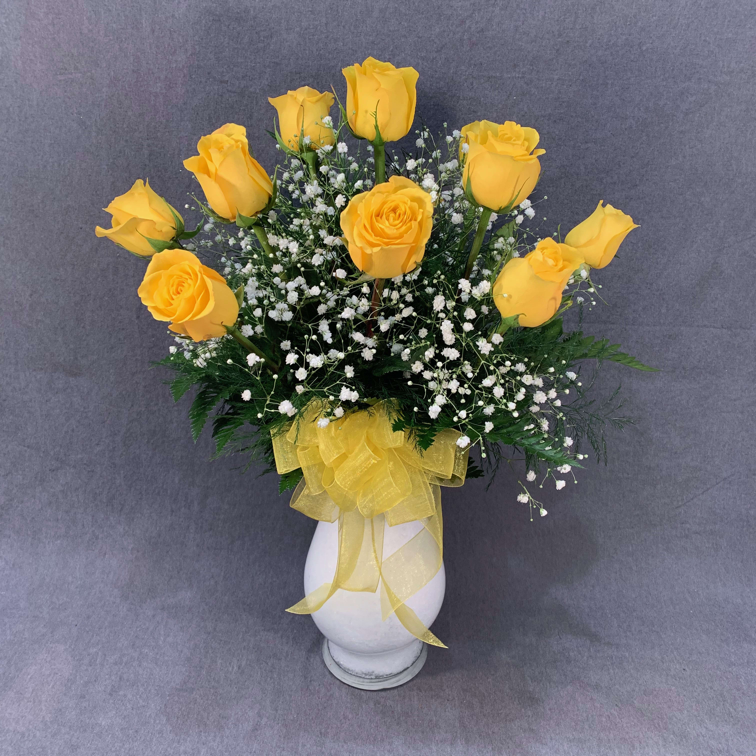 Yellow roses in a white vase with baby's breath and a yellow ribbon